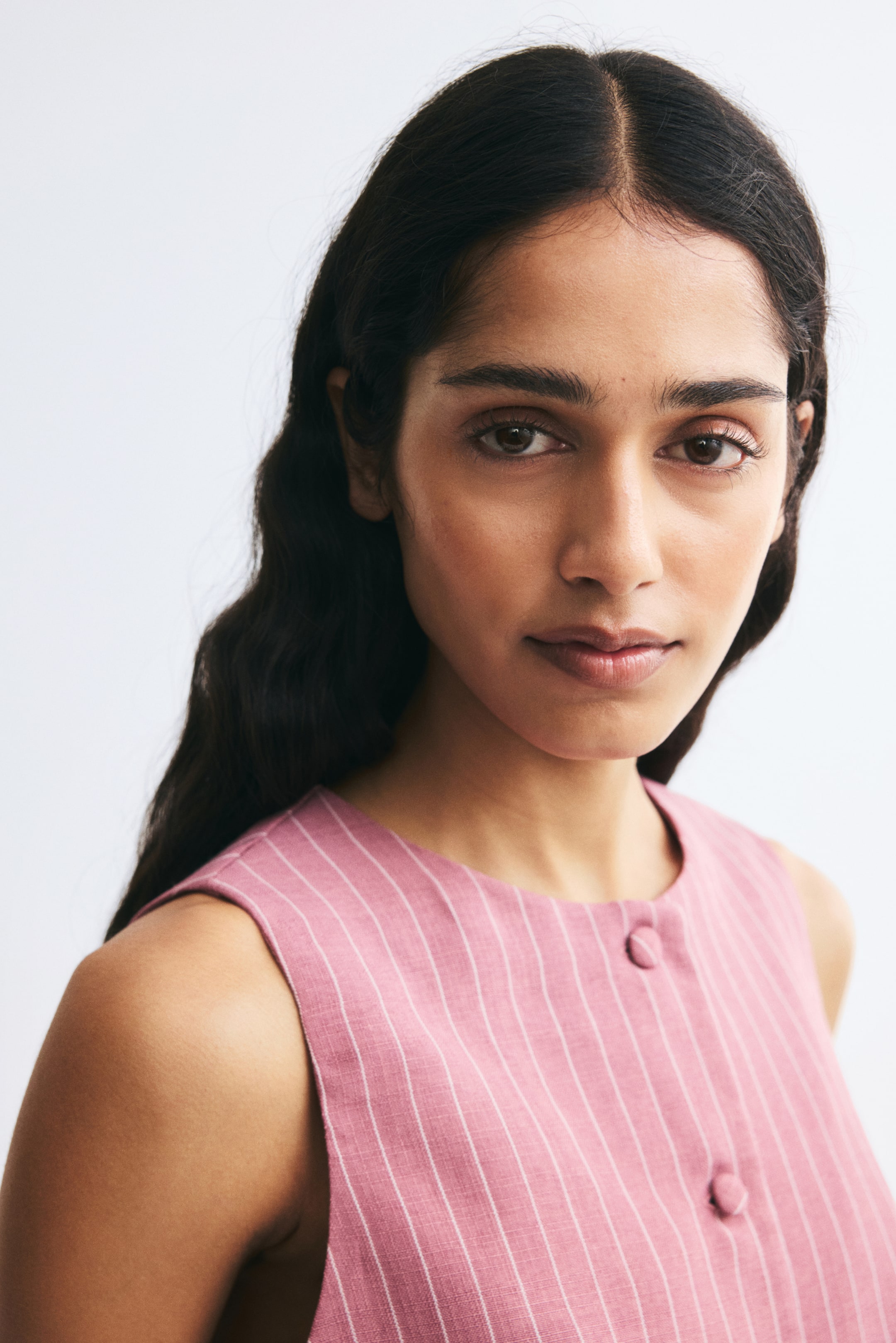 View larger image: A pink pinstriped waistcoat in a textured weave is shown from the front, featuring a round neckline and matching fabric-covered buttons.