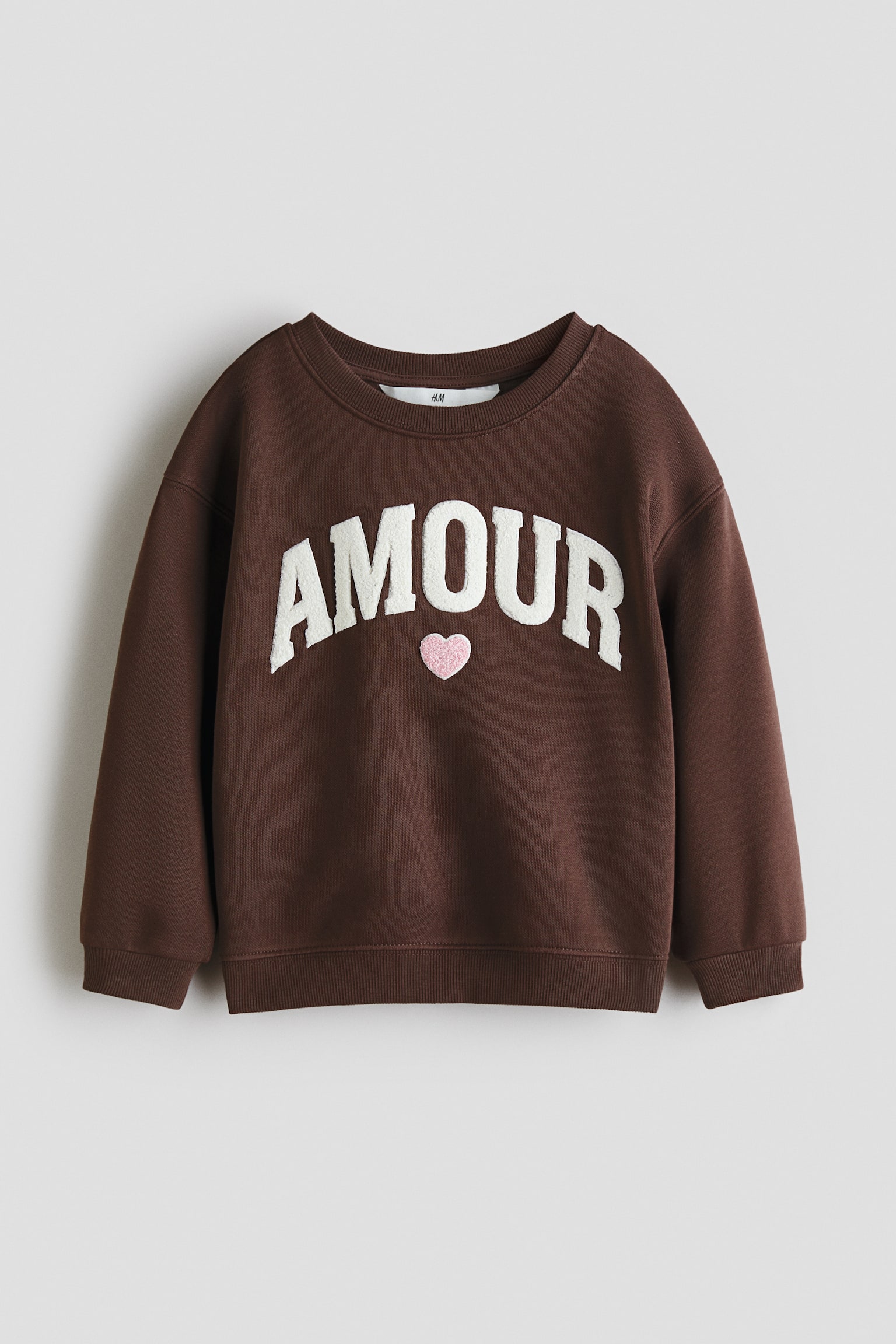 סווטשירט חום עם הכיתוב "AMOUR" באותיות טקסטורה לבנות ולב ורוד בחזית, כולל צווארון עגול עם צלעות, כתפיים נפולות, ומכפלת ושרוולים עם צלעות. - 1
