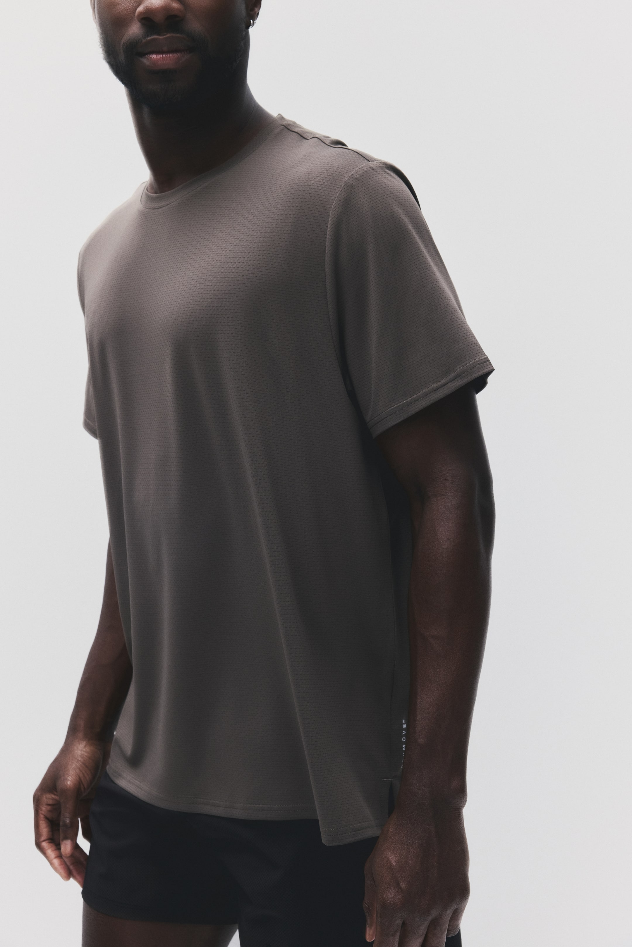 View larger image: The grey t-shirt features a fine textured knit and a crew neck, captured from a subtle front-left angle. Its short sleeves finish just above the elbow, with a small white 'ALL-MOVE?' logo visible on the lower left side.