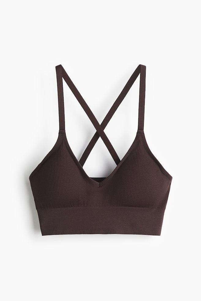 A dark brown Seamless Medium Support Sports bra with DryMove? is lying flat, presenting its front. It is featuring ribbed knit cups, a V-neckline, and a wide, smooth bottom band, with criss-cross straps visible behind the bra's body. - 1