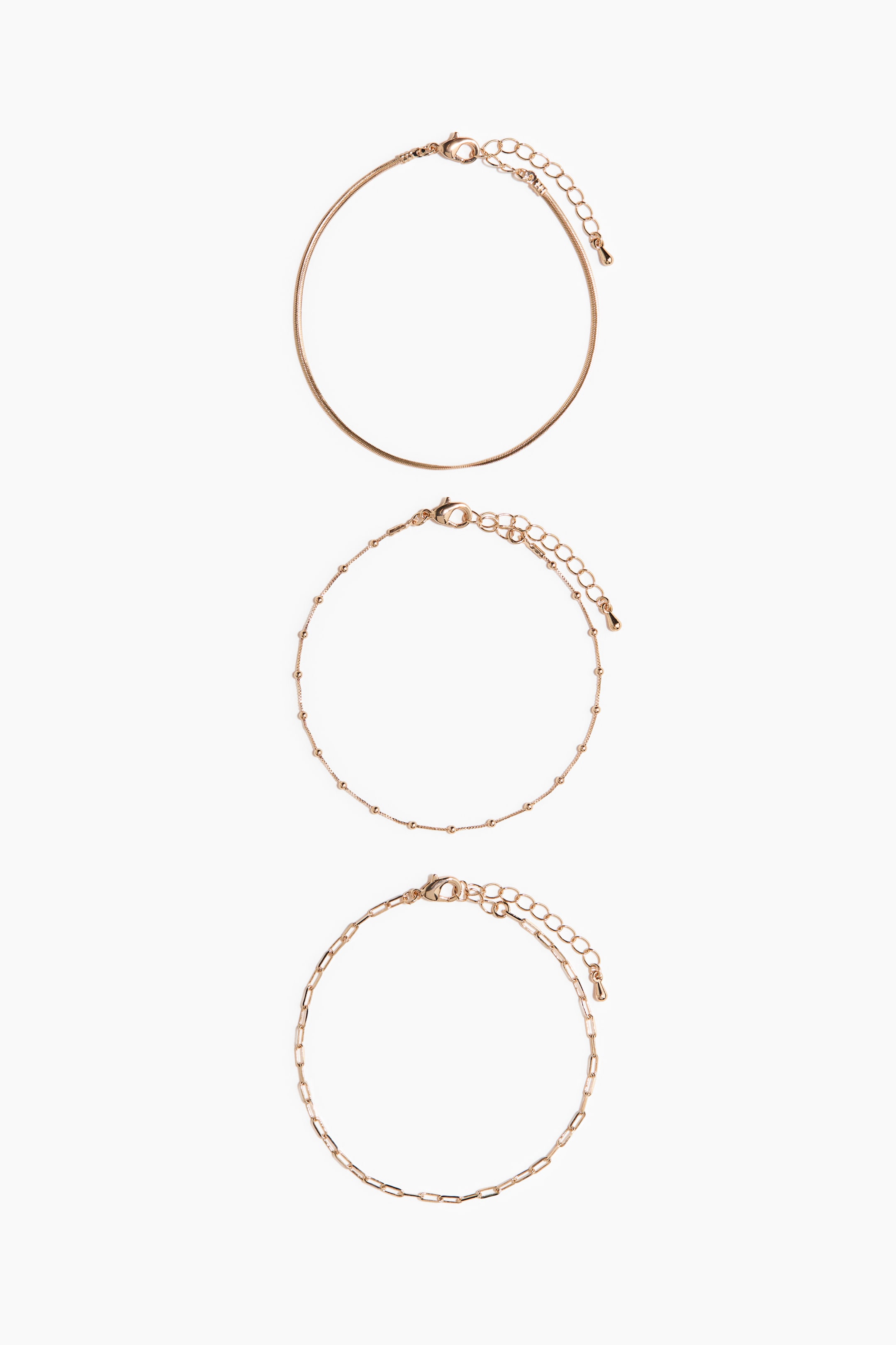 Grotere afbeelding bekijken: Drie goudkleurige armbanden liggen plat in een cirkelvorm, elk met hun ontwerp vanuit een vooraanzicht, voorzien van een karabijnsluiting en een verlengkettinkje. De bovenste armband heeft een gladde slangenketting, de middelste toont een verfijnde kralenketting en de onderste presenteert een paperclipketting.