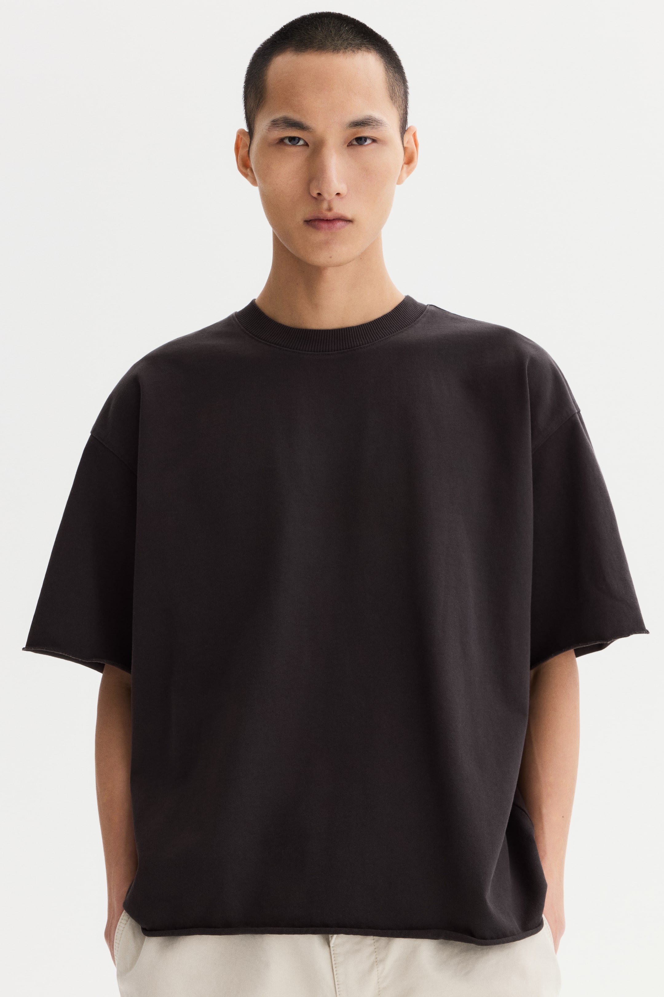 View larger image: A dark grey oversized short-sleeved top features a ribbed crew neck, dropped shoulders, wide raw-cut sleeve openings, and a raw-cut straight hem.