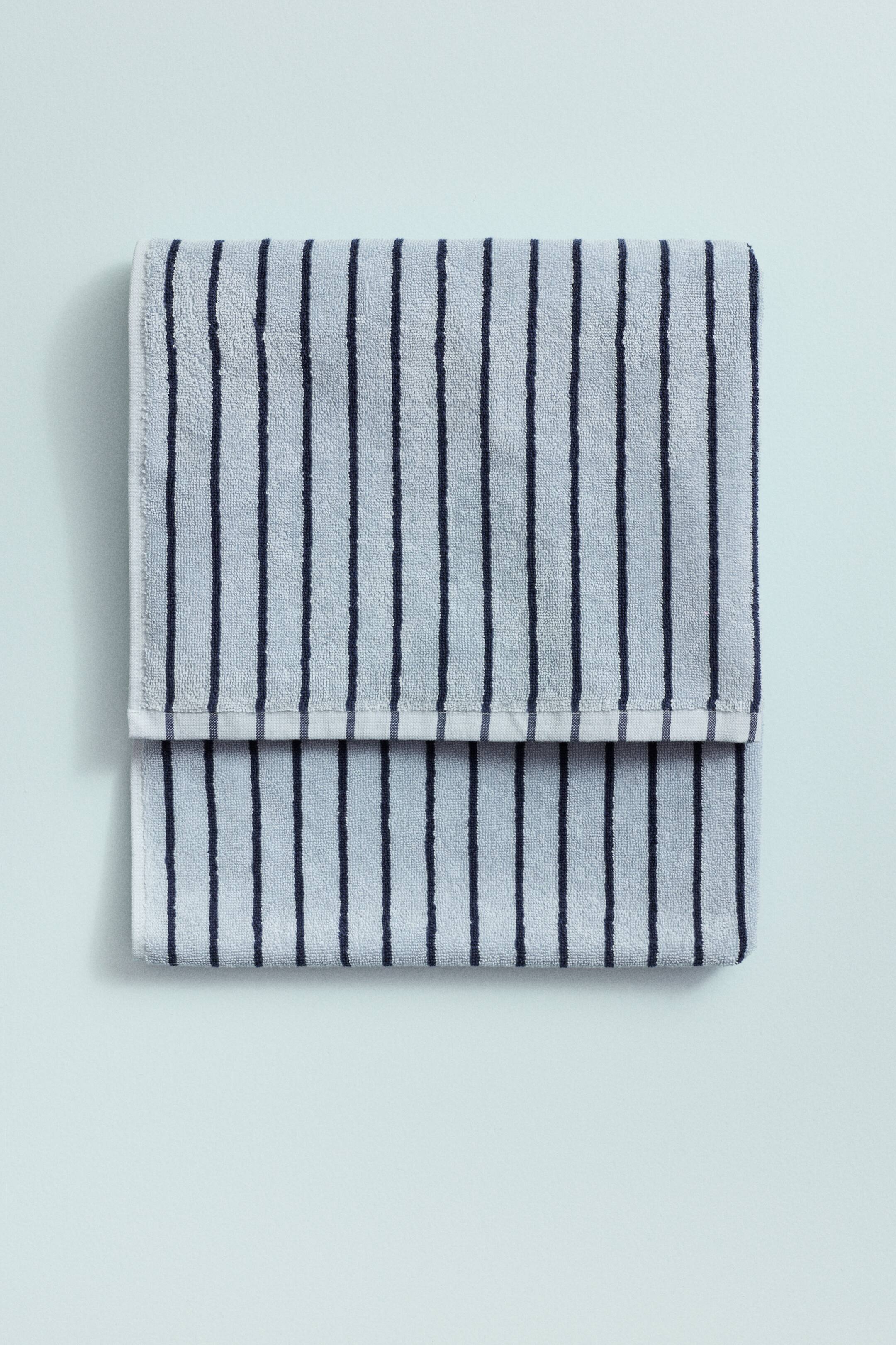 View larger image: A light blue terry cloth towel with dark blue vertical stripes is folded horizontally, revealing a white border along its fold line.