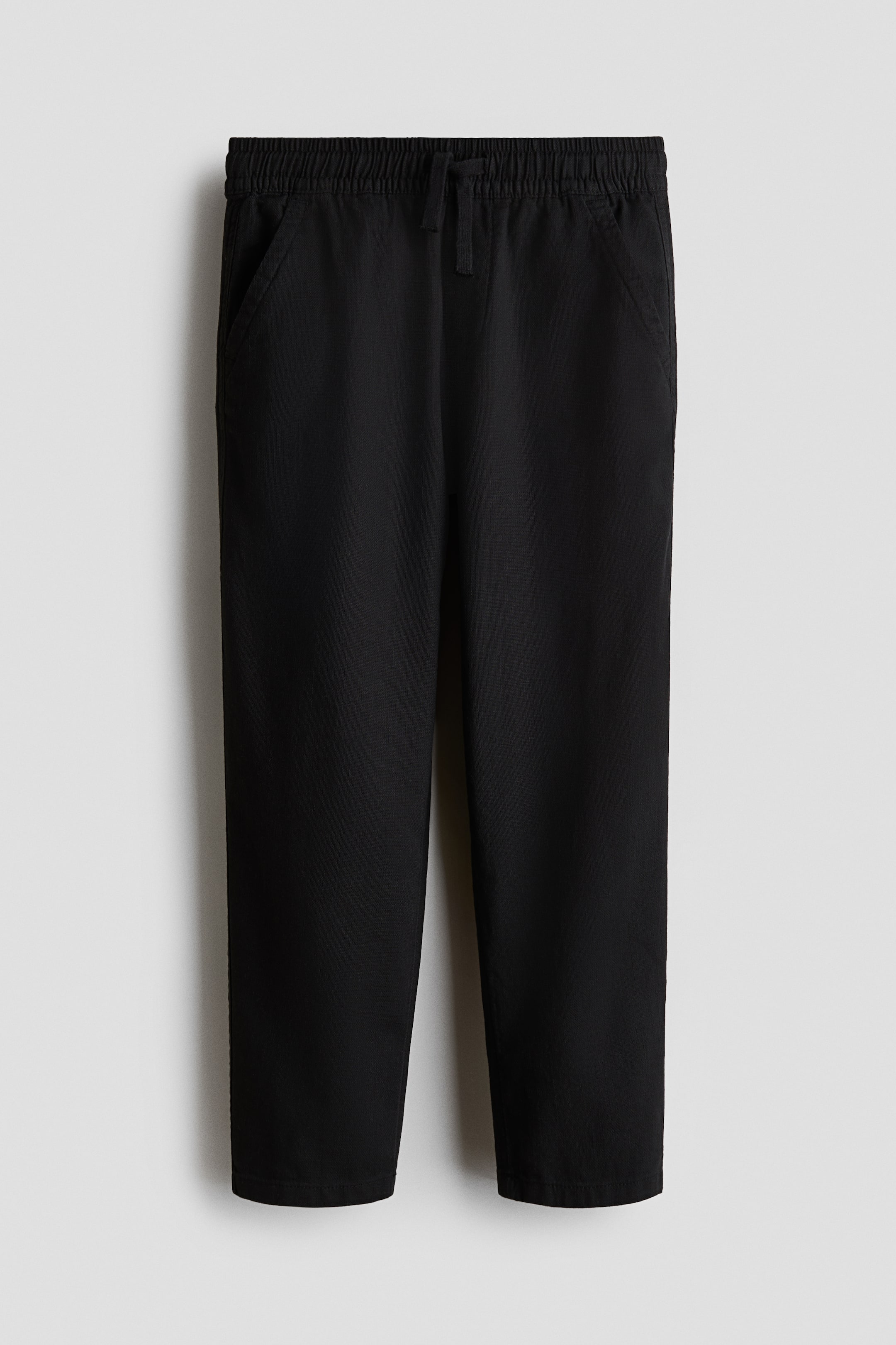 View larger image: Black pants are displayed from the front, featuring an elasticated waistband with a black drawstring. They come with two angled side pockets and straight legs with plain hems.