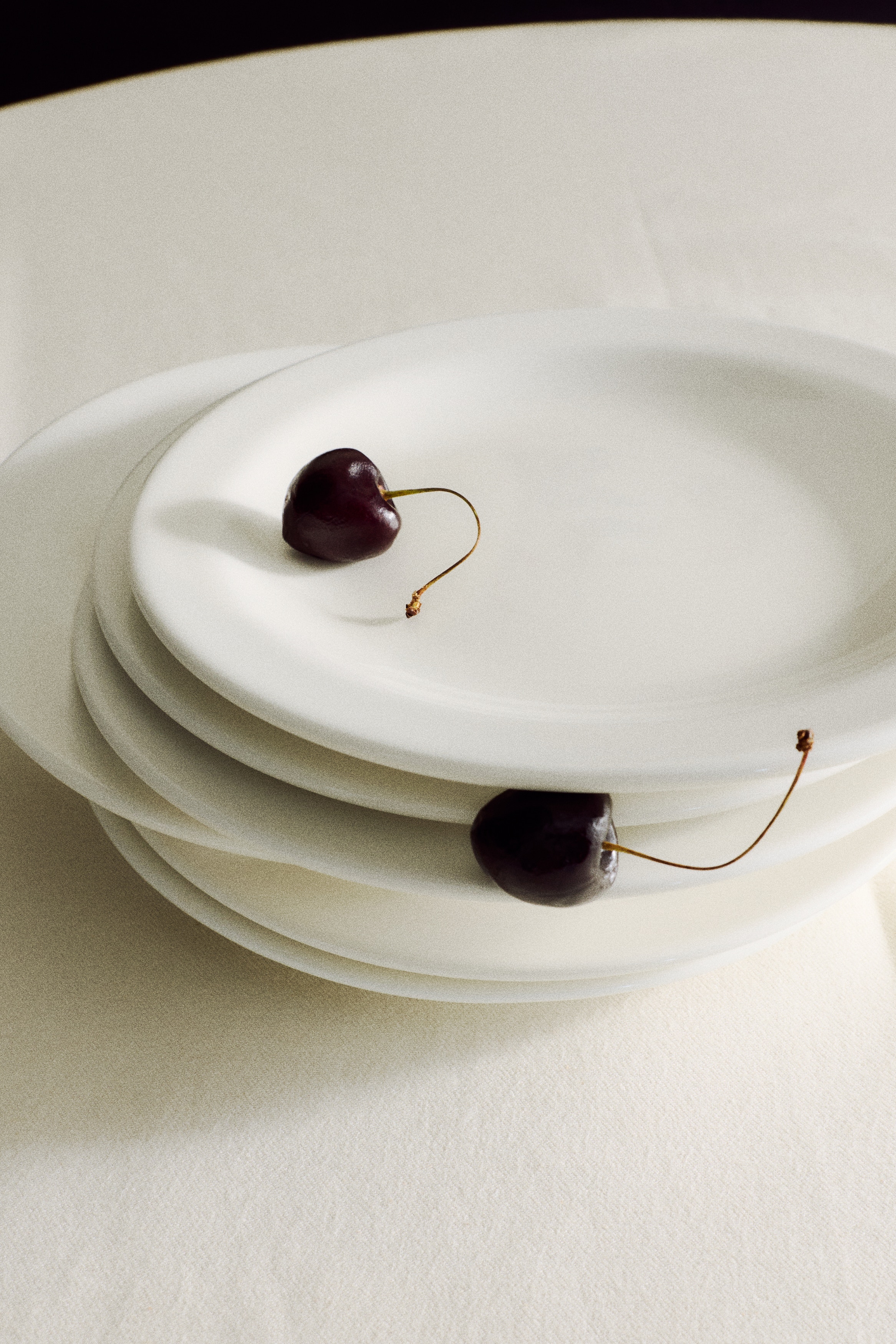 Two identical white round plates are lying flat and facing upwards, each featuring a slightly raised rim, and are positioned vertically one above the other.