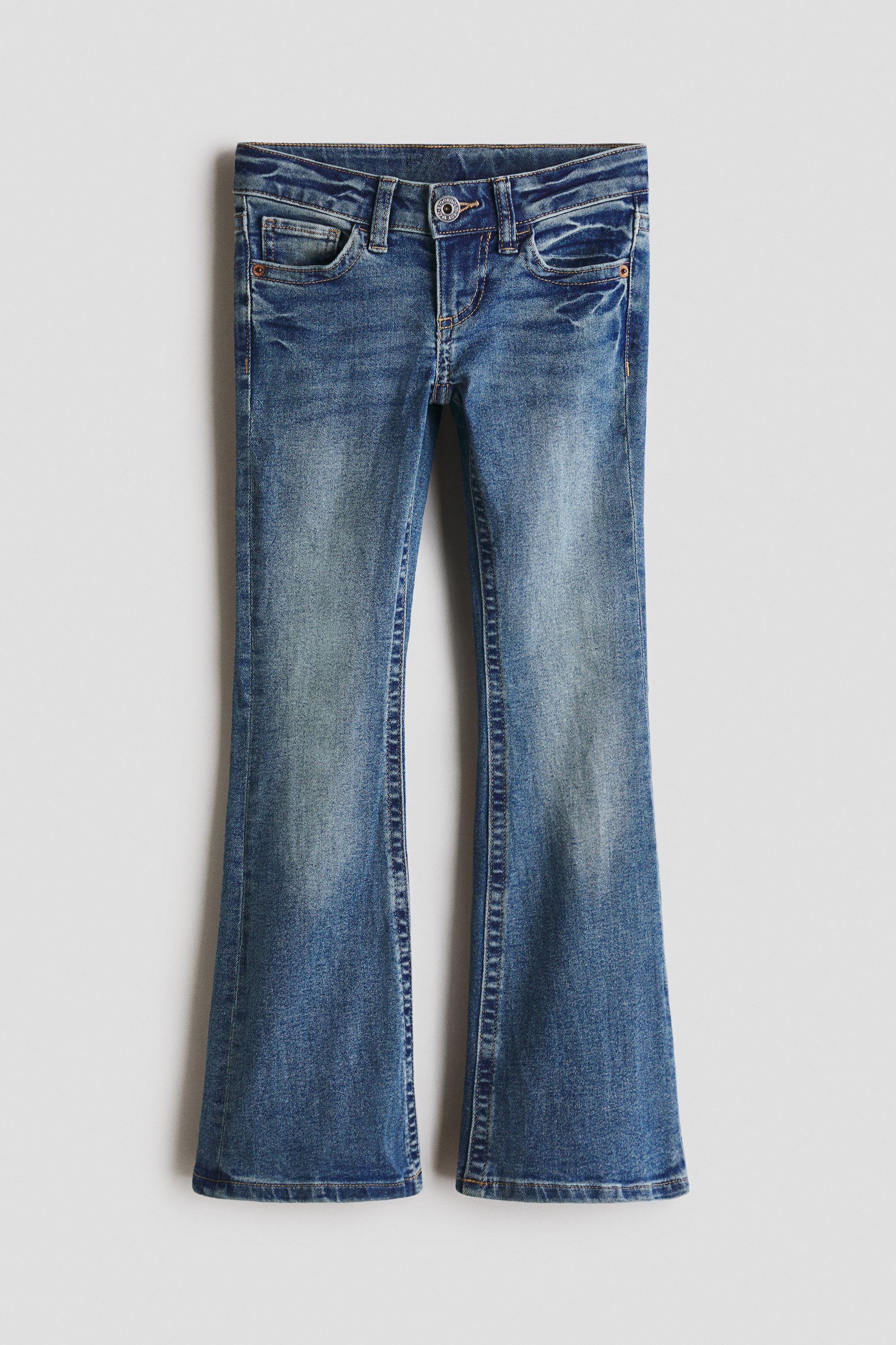 Ver imagen más grande: Unos vaqueros de denim azul medio están colocados en plano, mostrando una vista frontal, y presentan un lavado desgastado con cierre de botón y cremallera y trabillas para cinturón. Los vaqueros están diseñados con bolsillos delanteros tipo scoop y un pequeño bolsillo para monedas, ofreciendo un corte slim en los muslos que se ensancha hacia una abertura de pierna bootcut.