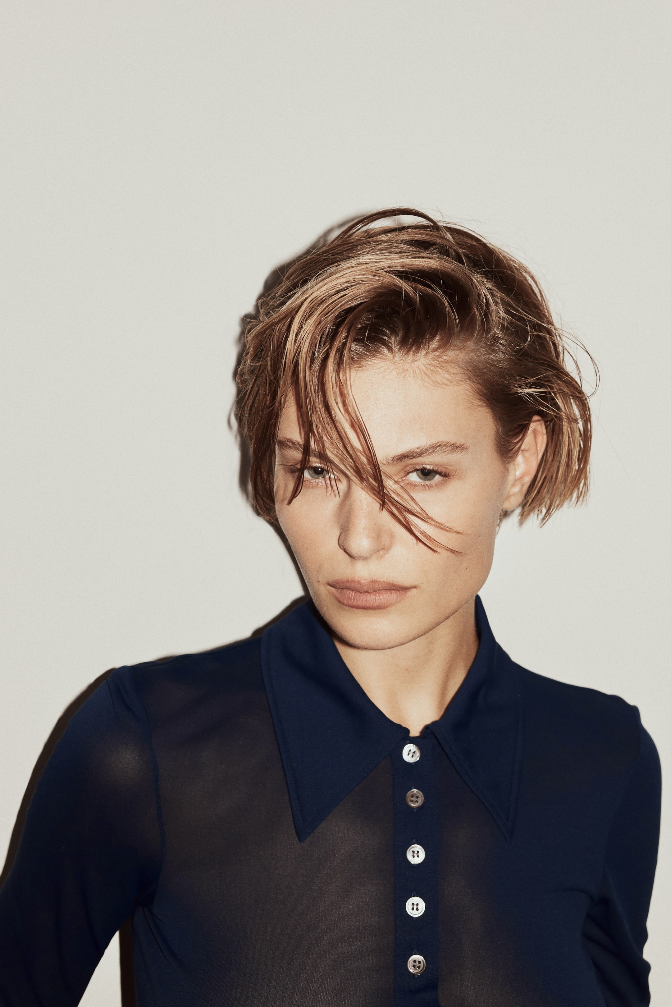 拡大画像を表示: ネイビーの長袖シャツは、透け感のある身頃と不透明な襟・前立て・袖を特徴としています。先の尖ったスプレッドカラーと、淡色の丸ボタンが5つ配された前立てを備えています。