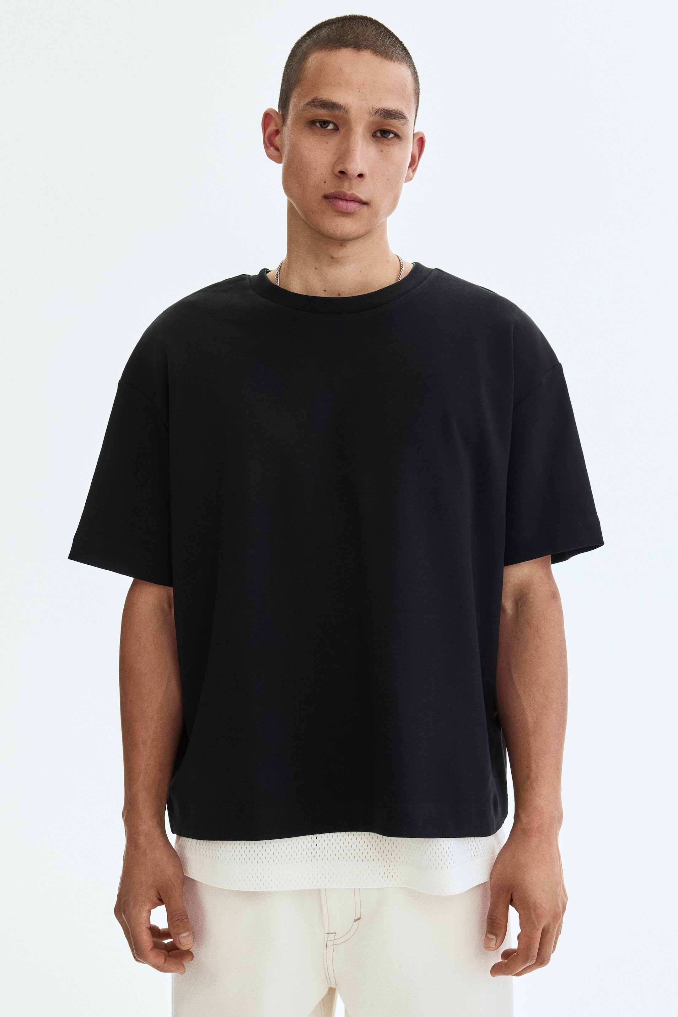 Größeres Bild anzeigen: Ein schwarzes T-Shirt mit Rundhalsausschnitt und kurzen, überschnittenen Ärmeln, das eine oversized Passform bietet. Eine weiße Mesh-Schicht zeigt sich unter dem geraden Saum.