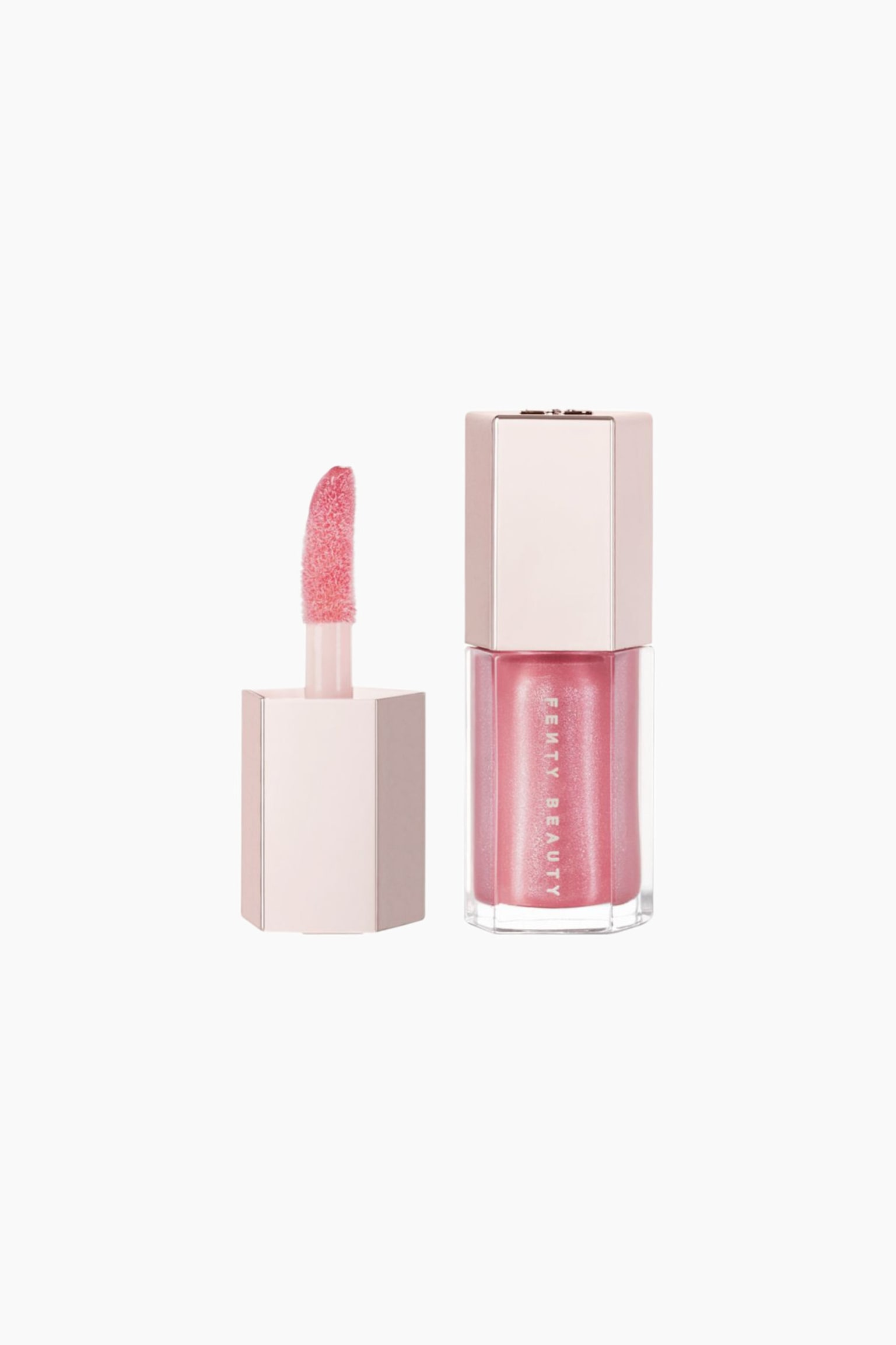 Mini Gloss Bomb Universal Lip Luminizer stÃ¥r oprejst og fremviser en hexagonal gennemsigtig flaske fyldt med skinnende pink gloss, afsluttet med et metallisk rosaguld lÃ¥g. Ved siden af flasken holder den matchende hexagonale hÃ¦tte staven oprejst og afslÃ¸rer en blÃ¸d, buet doe-foot-applikator dÃ¦kket af den samme skinnende pink formel.