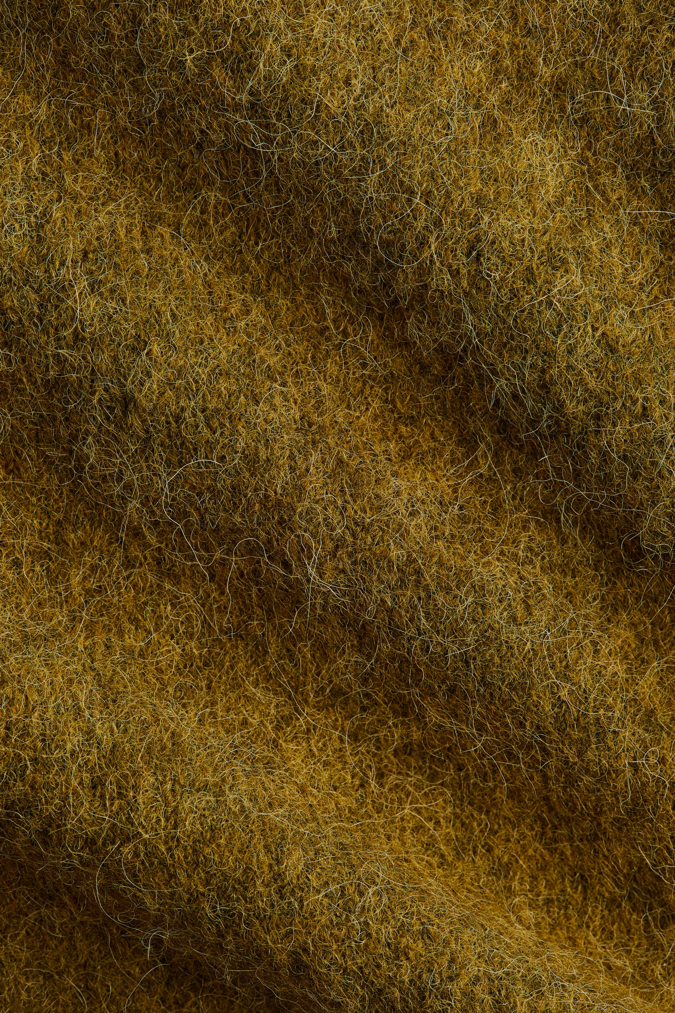 Agrandir l'image: Le tissu en maille douce d'un pull oversize, contenant de l'alpaga et de la laine, présente une surface texturée avec des fibres fines et visibles dans des tons terreux de jaune et de brun.