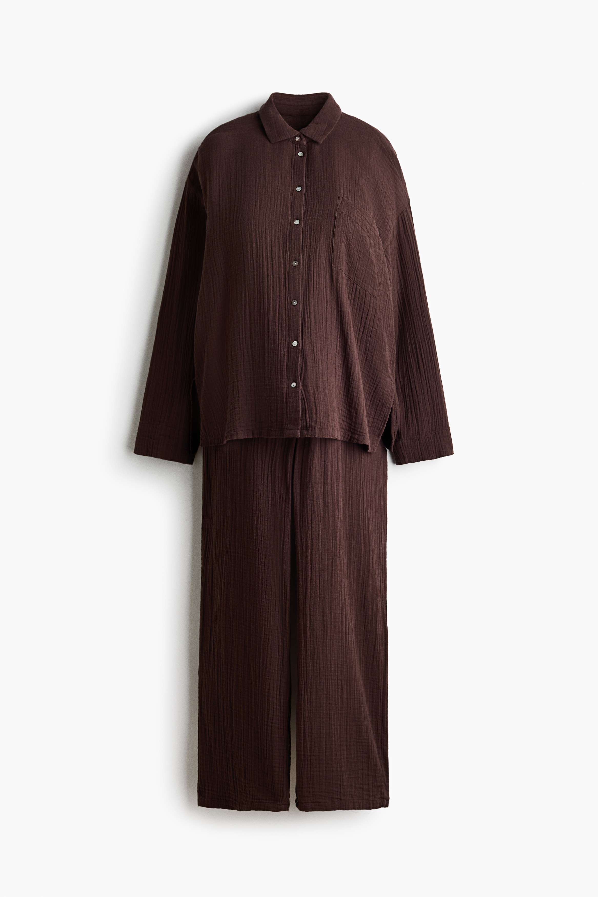 Un ensemble de loungewear Ã  texture froissÃ©e, de couleur marron foncÃ©, est portÃ© par le mannequin, qui ajuste le col de la chemise Ã  manches longues dâune main. Lâensemble se compose dâune chemise oversize boutonnÃ©e avec une poche poitrine et dâun pantalon large assorti Ã  coupe ample.