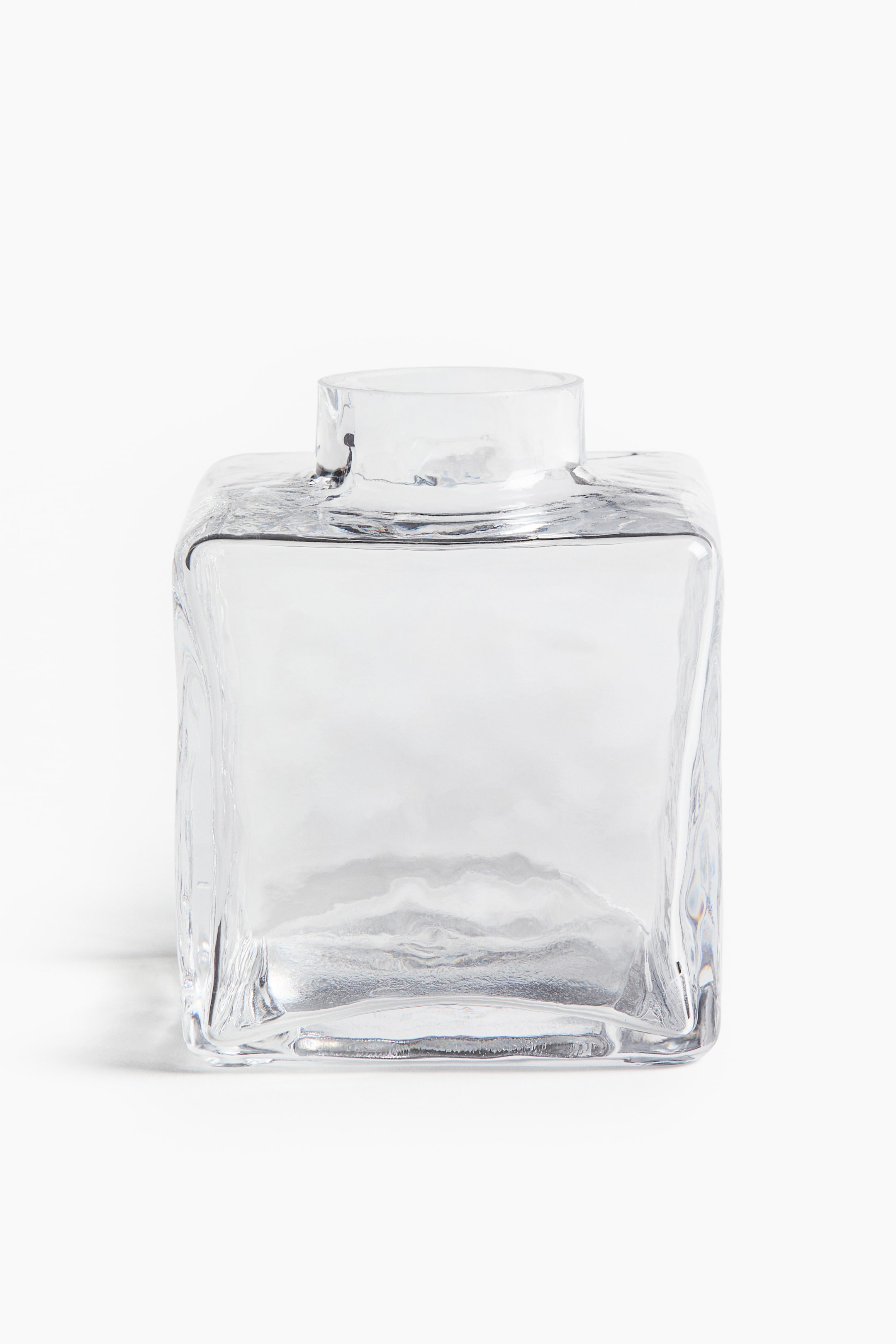 Zobrazit větší obrázek: Vázička na jednotlivé květy je zobrazena čelně jako čtvercová, čirá skleněná forma. Její povrchy mají výraznou, organickou texturu a z horní části vystupuje hladký, kruhový otvor.