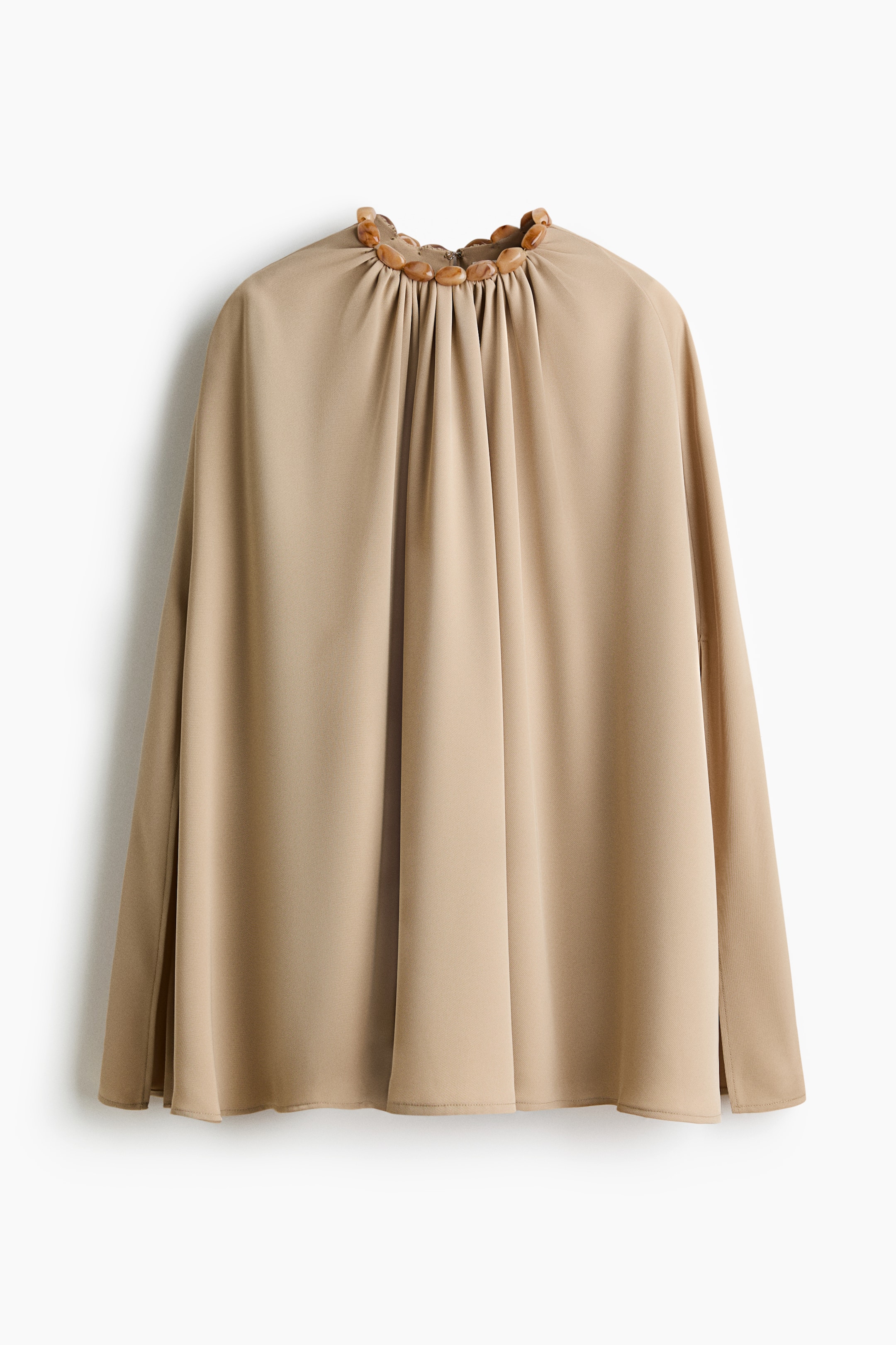 View larger image: A beige top is presenting FRONT, featuring a high gathered neckline that is adorned with a row of polished, amber-toned beads. The garment is designed with a loose, flowing silhouette and includes small side slits at the hem.