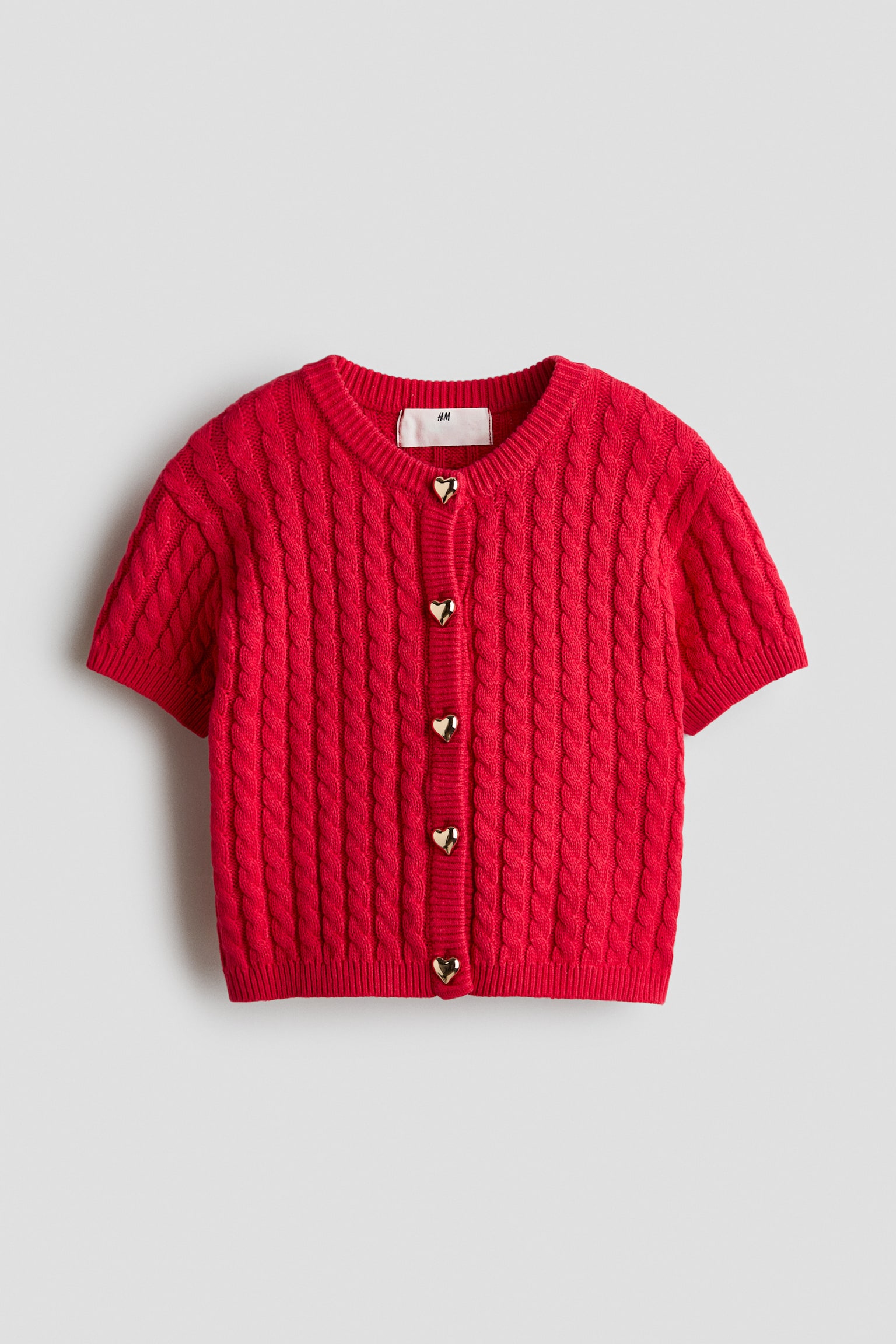 Má»t chiáº¿c Ã¡o cardigan dá»t kim há»a tiáº¿t cÃ¡p mÃ u Äá», tay ngáº¯n, Äang ÄÆ°á»£c chá»¥p chÃ­nh diá»n, vá»i cá» trÃ²n gÃ¢n vÃ  nÄm nÃºt hÃ¬nh trÃ¡i tim mÃ u vÃ ng Ã¡nh kim cháº¡y dá»c thÃ¢n trÆ°á»c. Ão cardigan cÃ³ bo gÃ¢n á» cá» tay vÃ  gáº¥u Ã¡o.