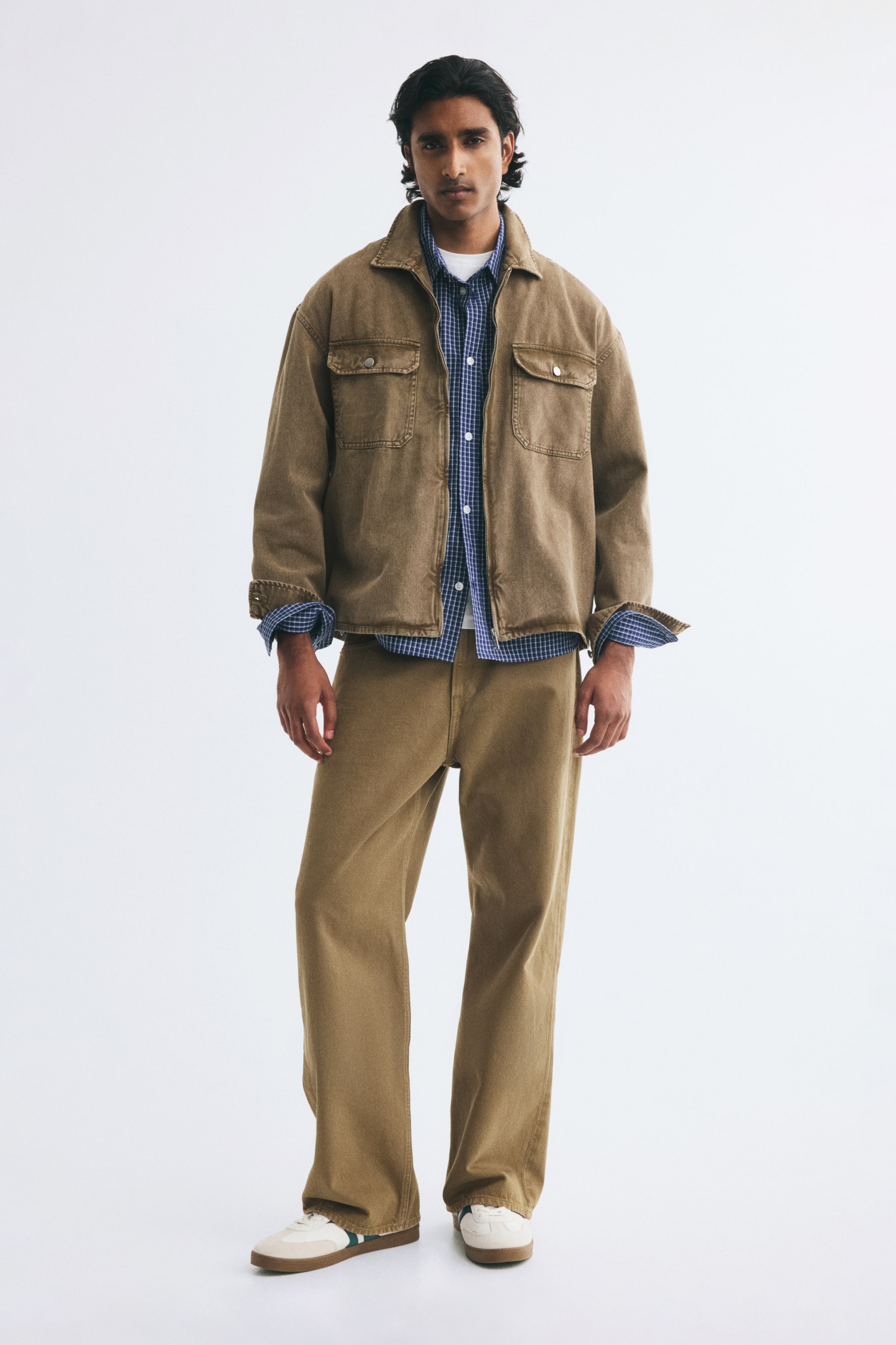 View larger image: Brown cotton denim jeans featuring a loose, straight-leg fit and a regular waist are worn by the model. The jeans are paired with a matching brown denim jacket, a blue checkered shirt, and white sneakers.