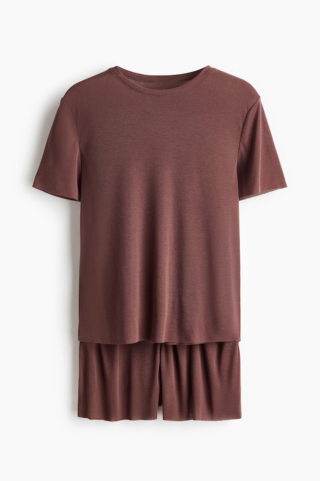 Ein braunes Pyjama-Set aus weichem Jersey präsentiert ein T-Shirt mit rundem, geripptem Ausschnitt und rohen Kanten an den Bündchen und am Saum. Die Shorts des Sets verfügen über einen elastischen Bund und Säume mit rohem Rand. - 1