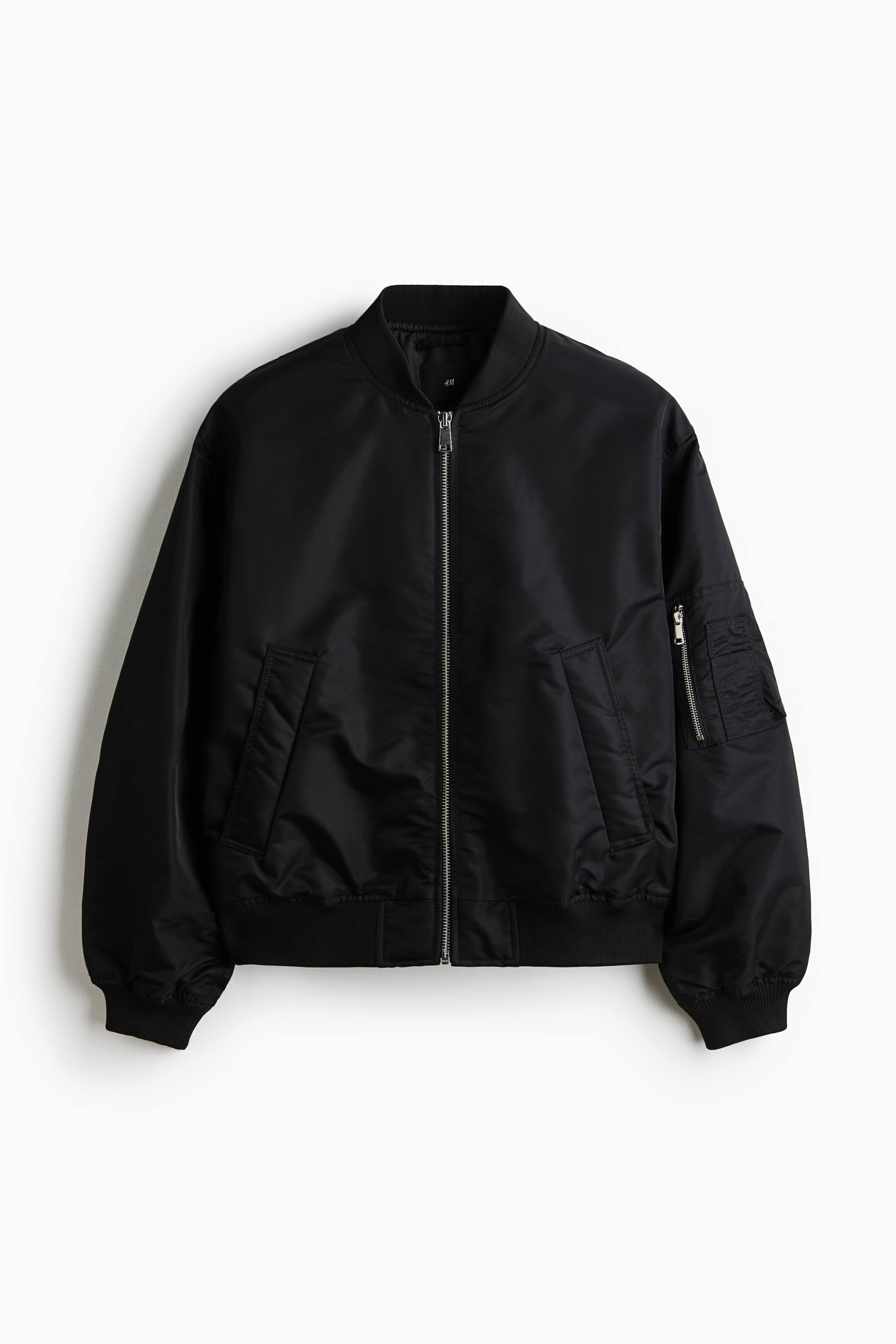 Ver imagen más grande: Se muestra una chaqueta bomber negra de frente, con una cremallera frontal en tono plateado, cuello alto acanalado, puños acanalados, dobladillo acanalado, dos bolsillos inclinados tipo ojal en la parte delantera y un bolsillo utilitario con cremallera y ranuras para bolígrafos en la manga izquierda.