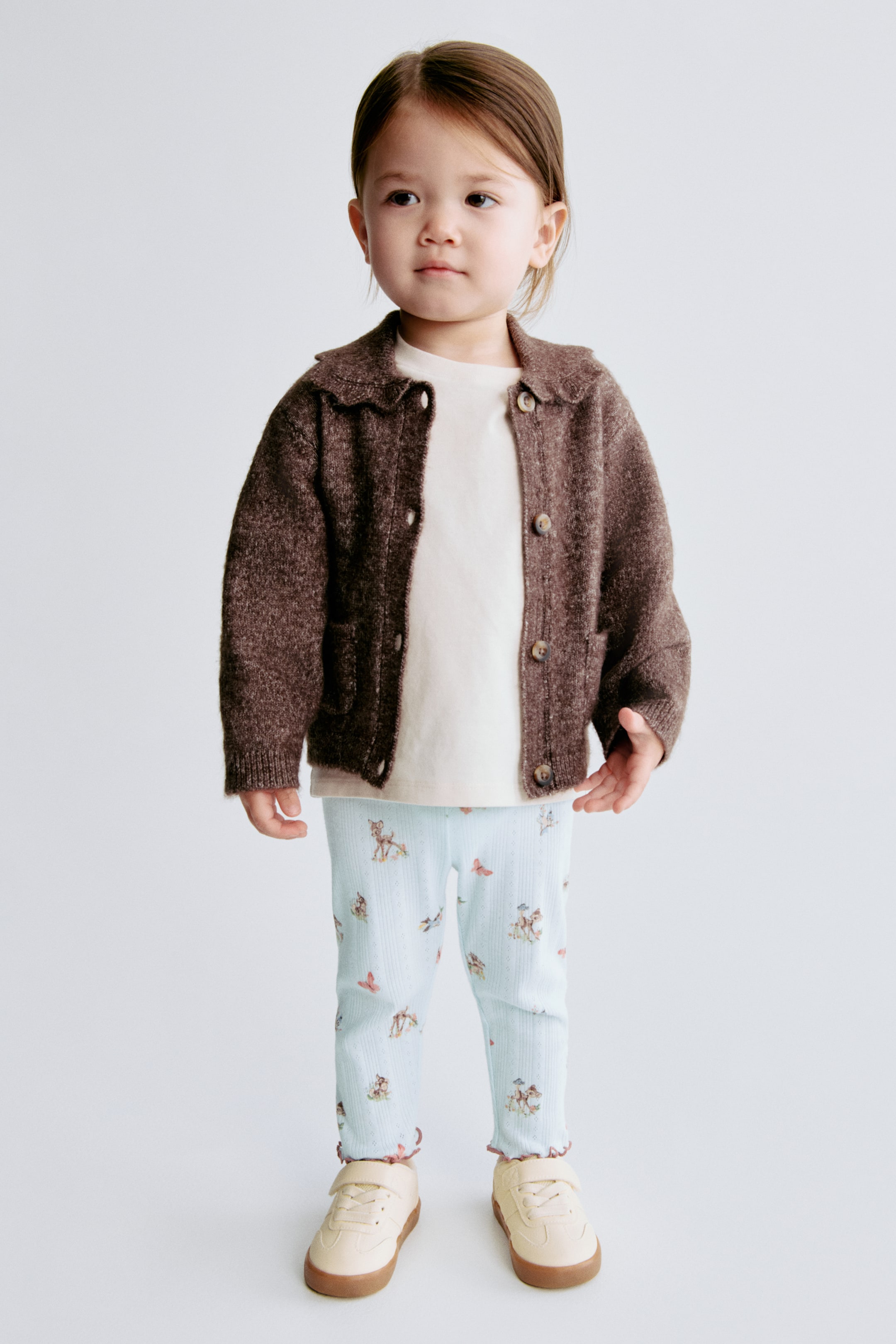 Agrandir l'image: Le cardigan marron présente une texture tricotée duveteuse et un col festonné. Il est conçu avec une fermeture à boutons sur le devant, deux poches plaquées et des poignets côtelés, et est superposé à un haut de couleur crème.