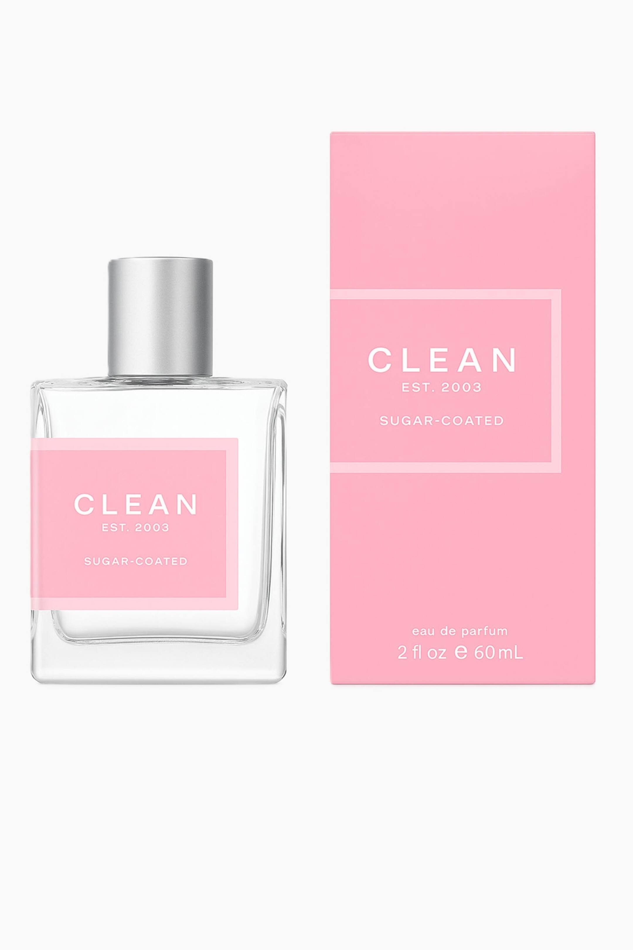 Vis større bilde: En klar, rektangulær parfymeflaske med en sølvkork og en rosa etikett med påskriften "CLEAN EST. 2003 SUGAR-COATED" står vendt forfra ved siden av sin matchende rosa rektangulær eske, som viser samme tekst samt "eau de parfum 2 fl oz e 60 mL".