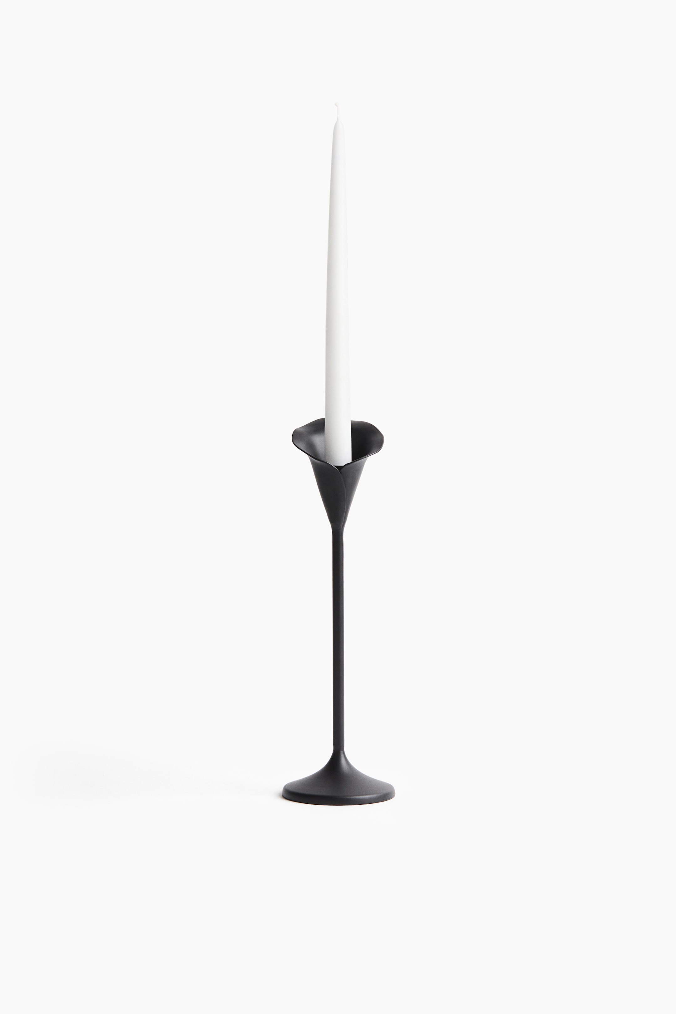 View larger image: A black metal candle holder is holding a white taper candle. The holder is designed with a round base, a slender stem, and an organically flaring cup.