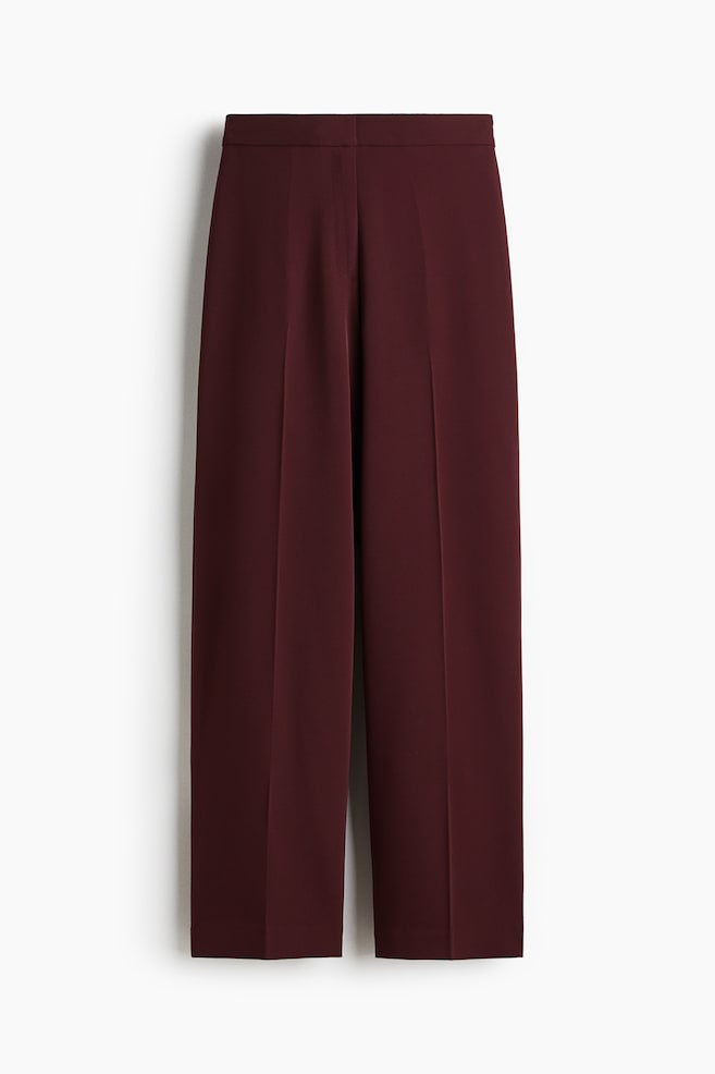 Front view of a pair of maroon straight-leg trousers, featuring a flat waistband and prominent pressed creases running down the center of each leg. - 1