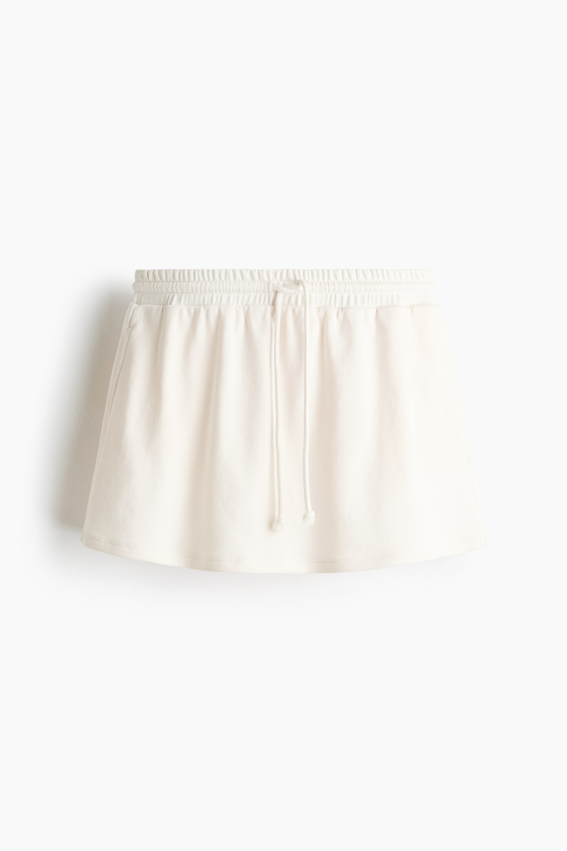 View larger image: A mini skort in light cream, lightweight sweatshirt fabric is displayed from the front. It highlights an elasticated drawstring waist, with the drawstring visibly tied at the center front.