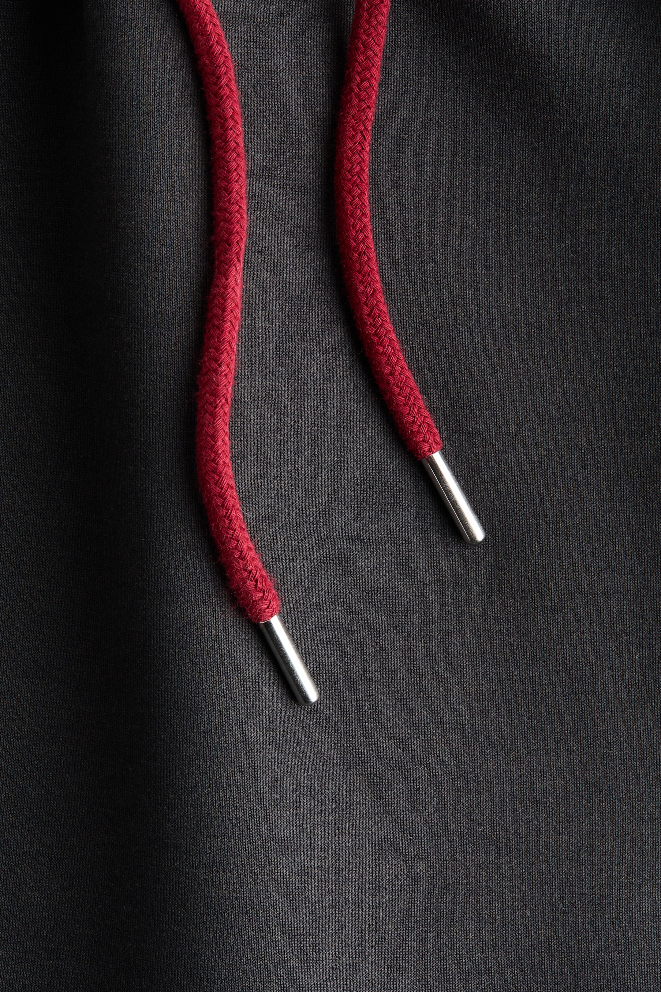 拡大画像を表示: ダークグレーのニット生地には、2本の赤い編み紐があり、それぞれがシルバートーンの金属チップで終わっています。