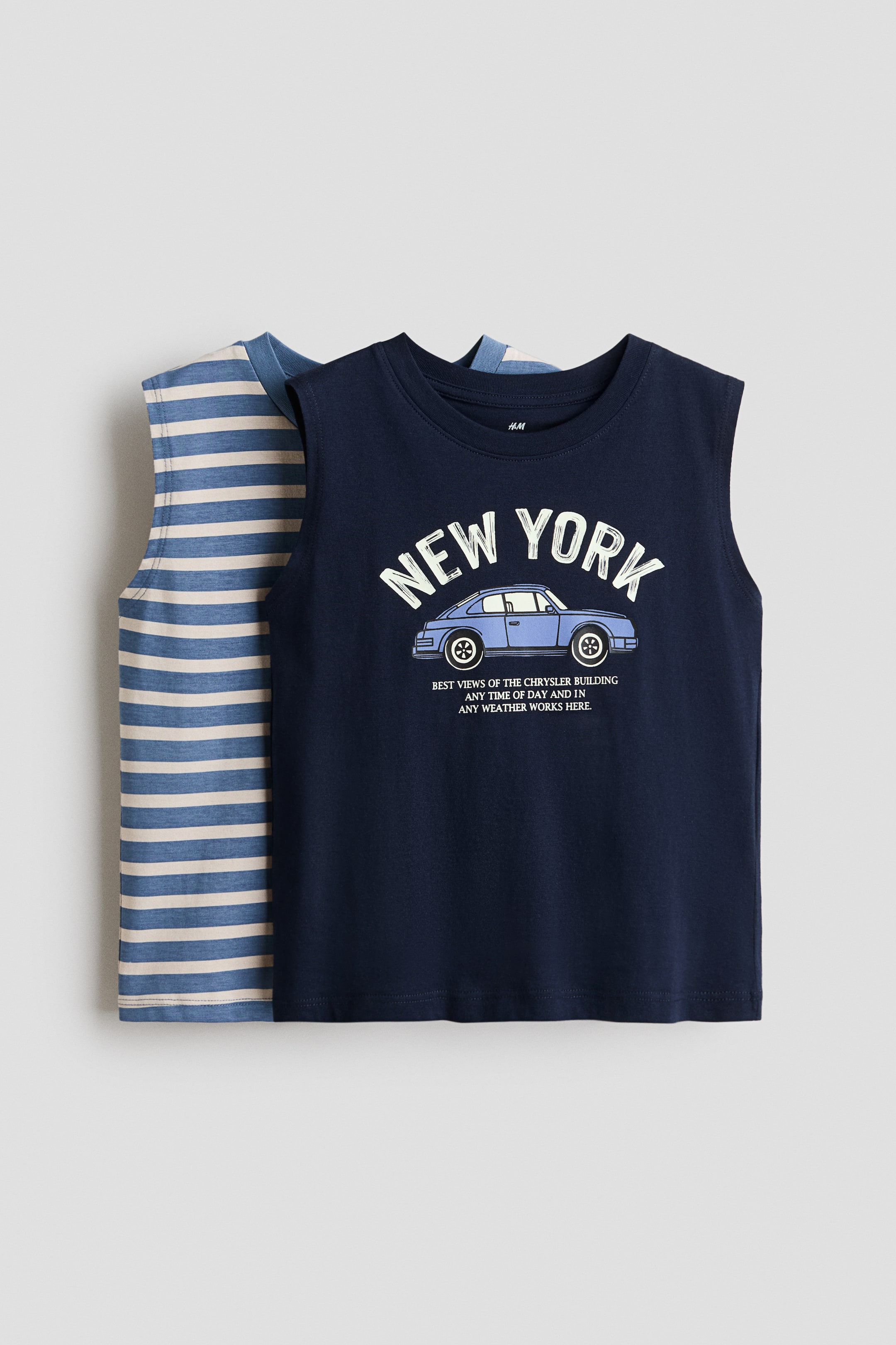 View larger image: Dalawang sleeveless tops ang ipinapakita, kung saan ang isa ay bahagyang nakapatong sa likod ng isa. Ang nasa harap na top ay navy blue at mayroong puting 'NEW YORK' na graphic sa ibabaw ng isang light blue na classic car, na may maliit na puting teksto na nakalimbag sa ibaba ng kotse. Ang top sa likod nito ay nagpapakita ng pahalang na stripes sa light blue at beige.
