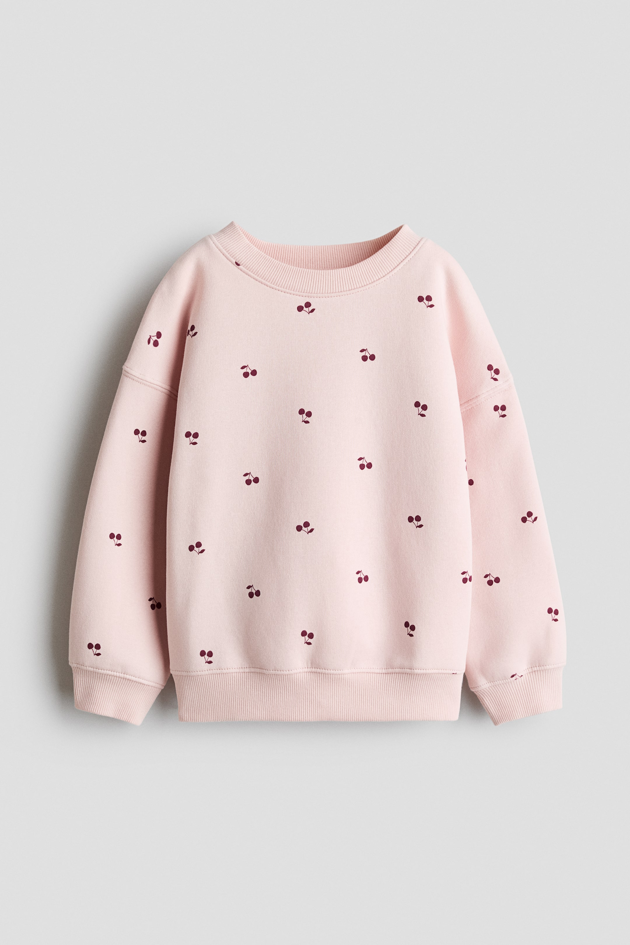 View larger image: A pink sweatshirt features an allover dark red cherry print. It is designed with a crew neck, long sleeves with ribbed cuffs, and a ribbed hem, shown from the front.