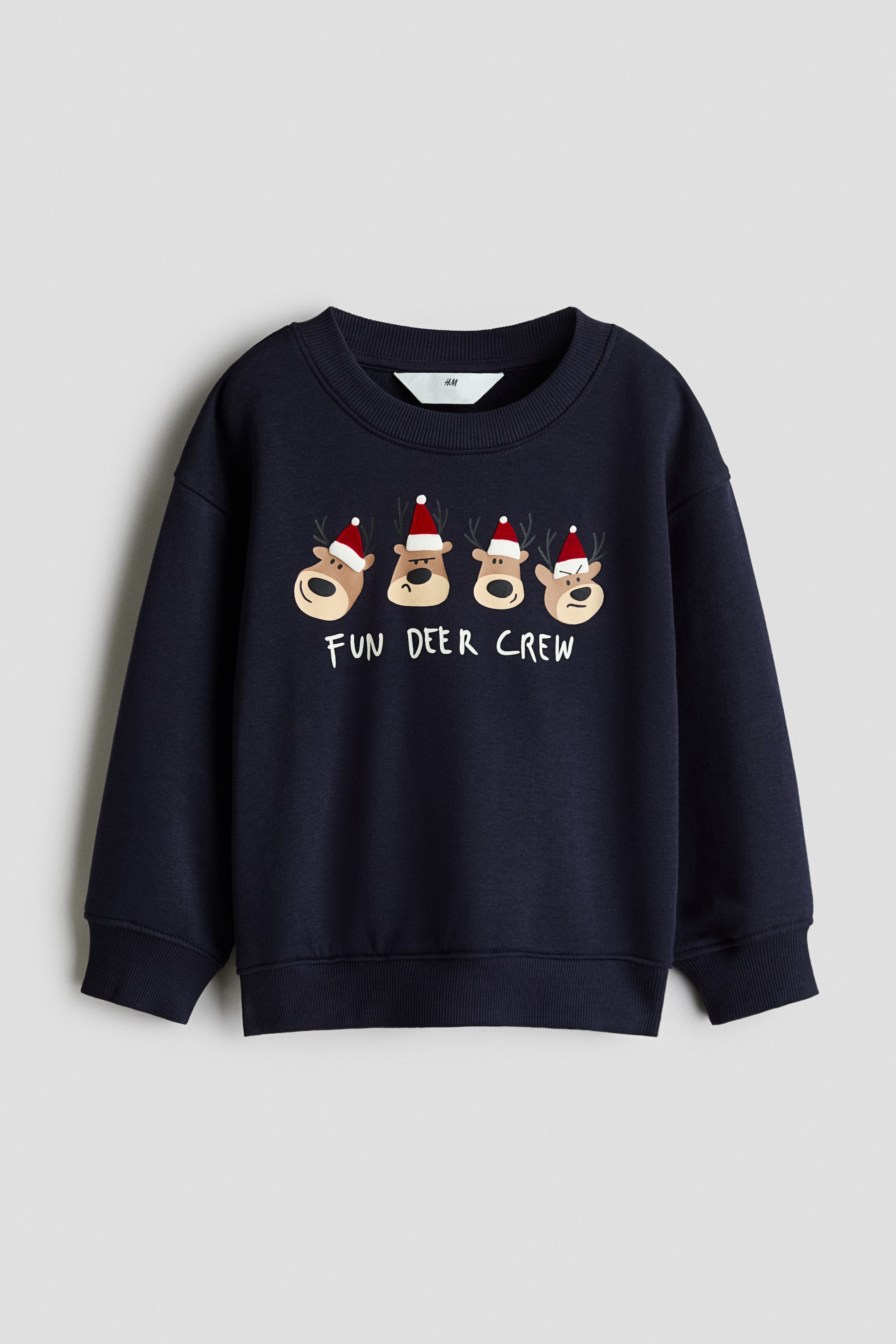 Größeres Bild anzeigen: Ein navyblauer Sweatshirt ist von vorne zu sehen und zeigt einen Grafikdruck mit vier gezeichneten Rentieren mit roten Weihnachtsmützen über dem weißen Schriftzug „FUN DEER CREW“. Das Kleidungsstück ist mit einem gerippten Rundhalsausschnitt, überschnittenen Schultern sowie gerippten Bündchen und Saum gestaltet.