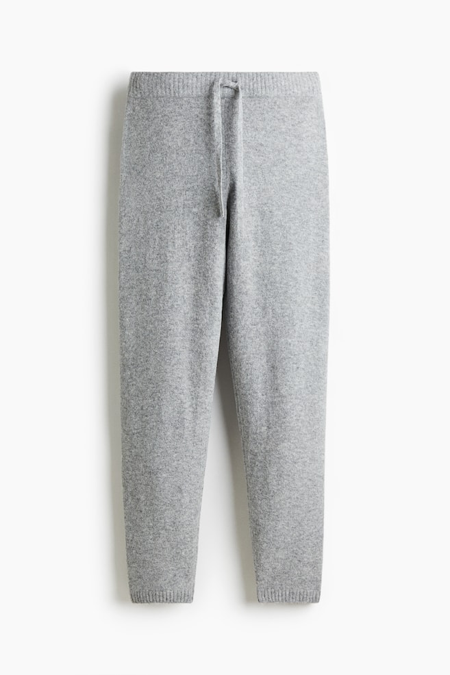 Grijze joggers worden gepresenteerd in een VOORAANZICHT, met een fijne breistructuur. De tailleband heeft een zichtbare trekkoord en de pijpen lopen taps toe naar geribbelde zomen. - 1