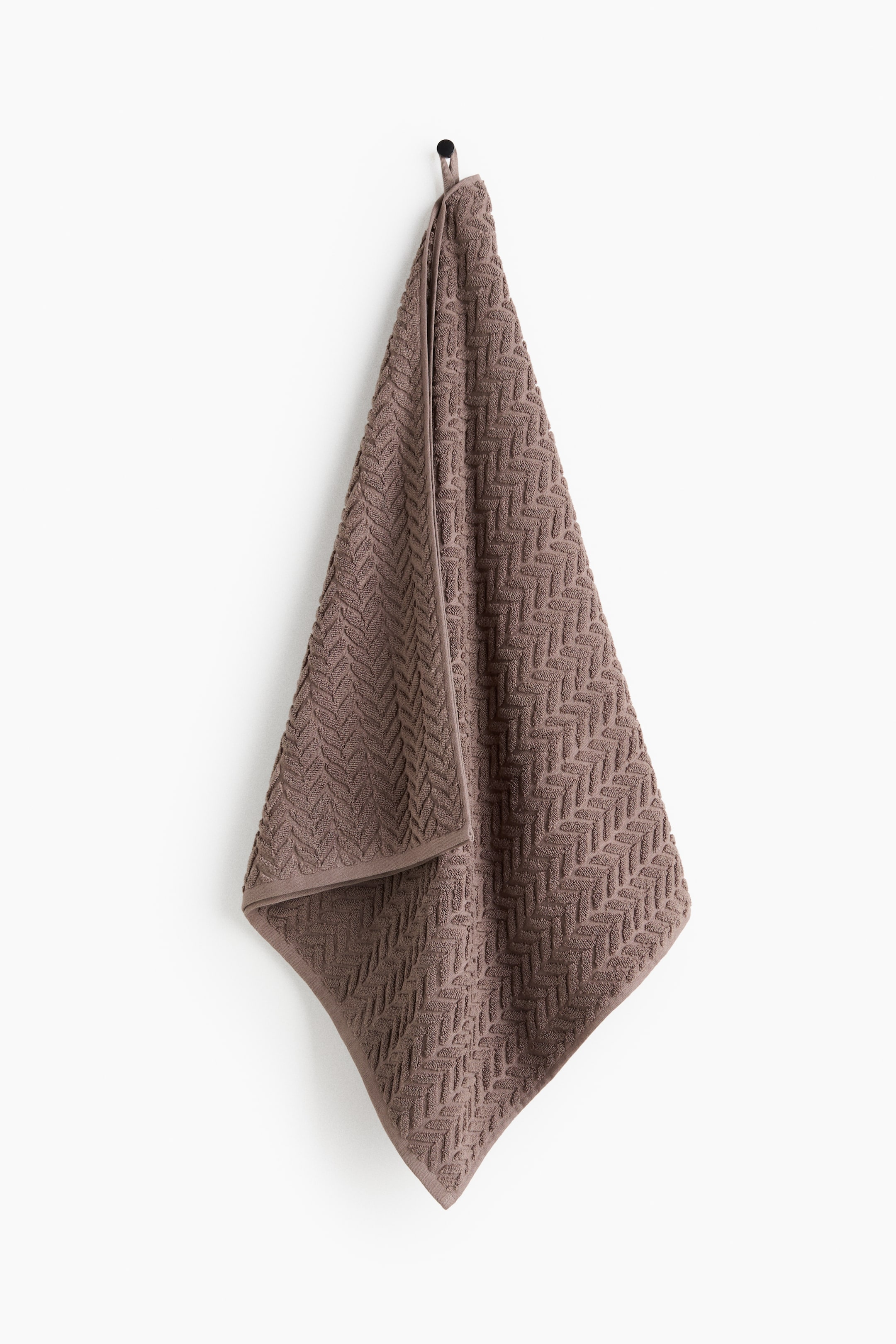 View larger image: A brown bath towel is hanging, showcasing its plush cotton terry fabric with a textured, cable knit-inspired pattern. A hanger loop is visible at the top on one long side.