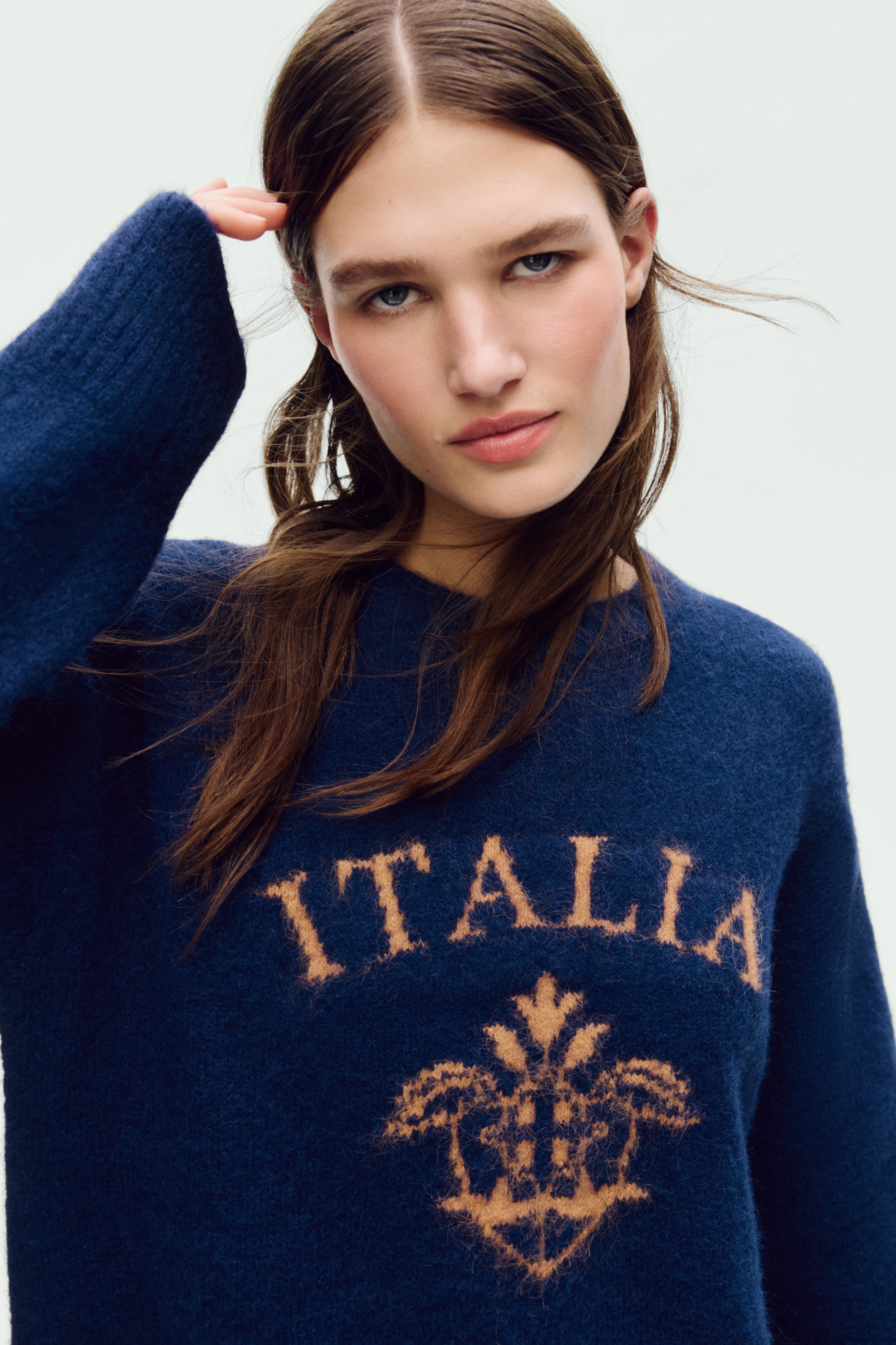 View larger image: A dark-blue, textured crew-neck sweater features the word 'ITALIA' in light-brown, fuzzy lettering across the chest, with a matching decorative crest positioned below it and angled slightly to the right.