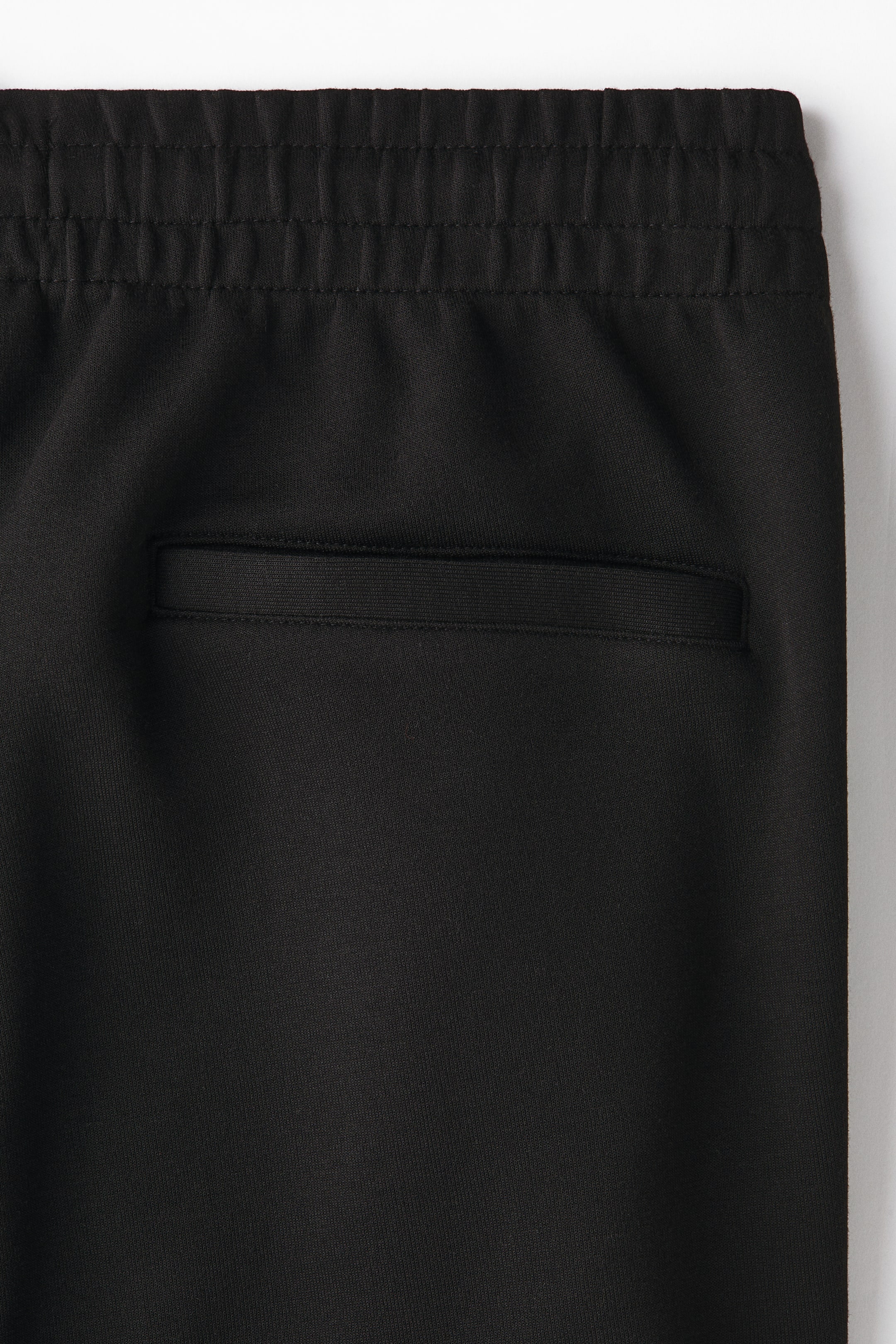 View larger image: Black trousers are featuring an elasticated, gathered waistband, below which a horizontal welt pocket is positioned, showcasing a ribbed trim along its opening.