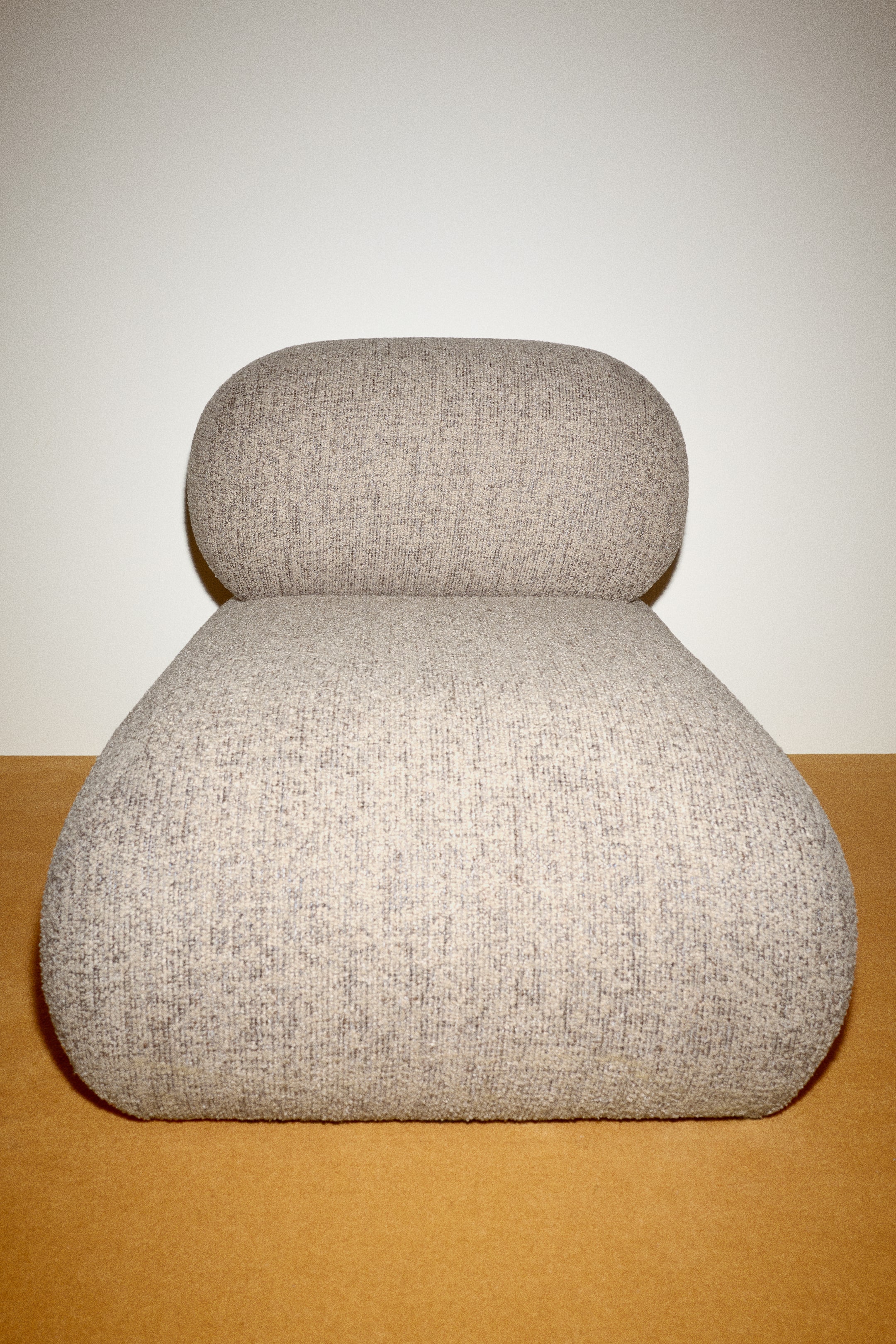Ver imagen más grande: La silla de acento Poma presenta un cojín de asiento amplio y redondeado y un cojín de respaldo más pequeño y redondeado, que descansa directamente sobre el asiento. Ambos cojines están tapizados en una tela texturizada de color gris claro con motas oscuras visibles.