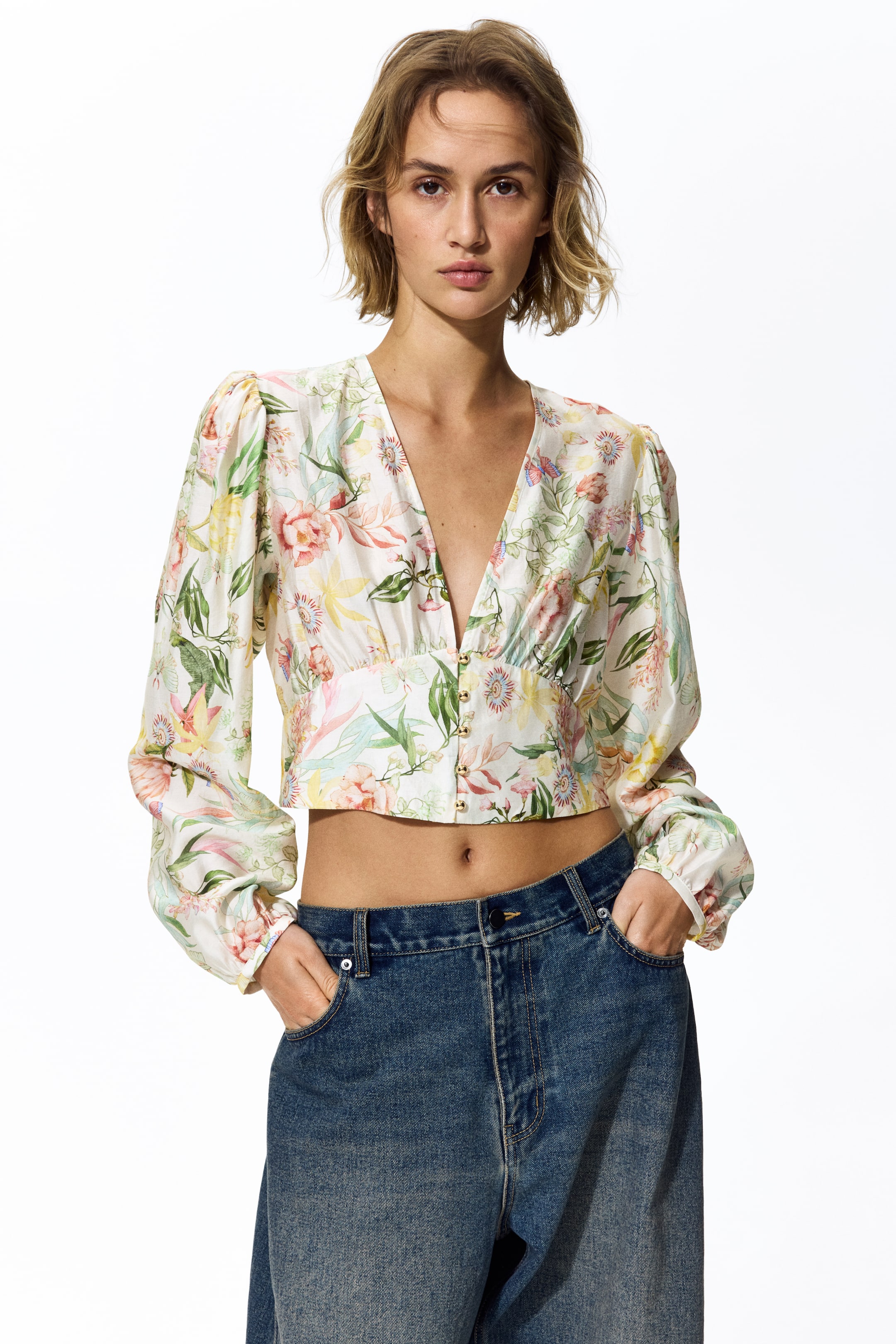 Visa större bild: En flerfärgad blommig crop top med ett djupt V-ringning och långa ärmar med puffiga axlar, samlade vid manschetterna. Guldtonade hyska och hake-stängningar säkrar den främre bodicen, som är samlad ovanför den raka korta fållen.
