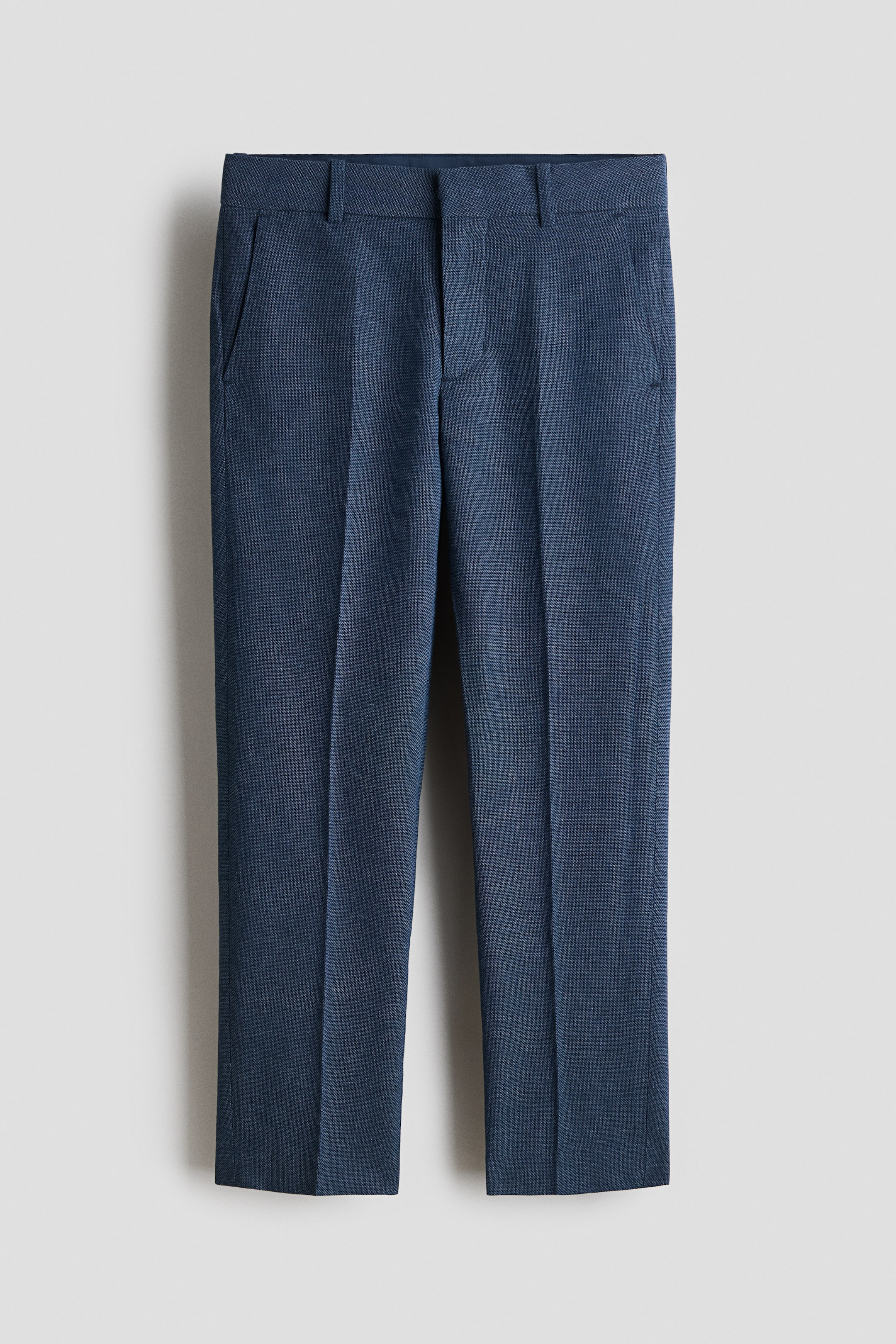 View larger image: The blue trousers showcase a textured woven fabric at the front, featuring a flat front, a waistband with belt loops, angled side pockets, and sharp vertical creases running down each leg.