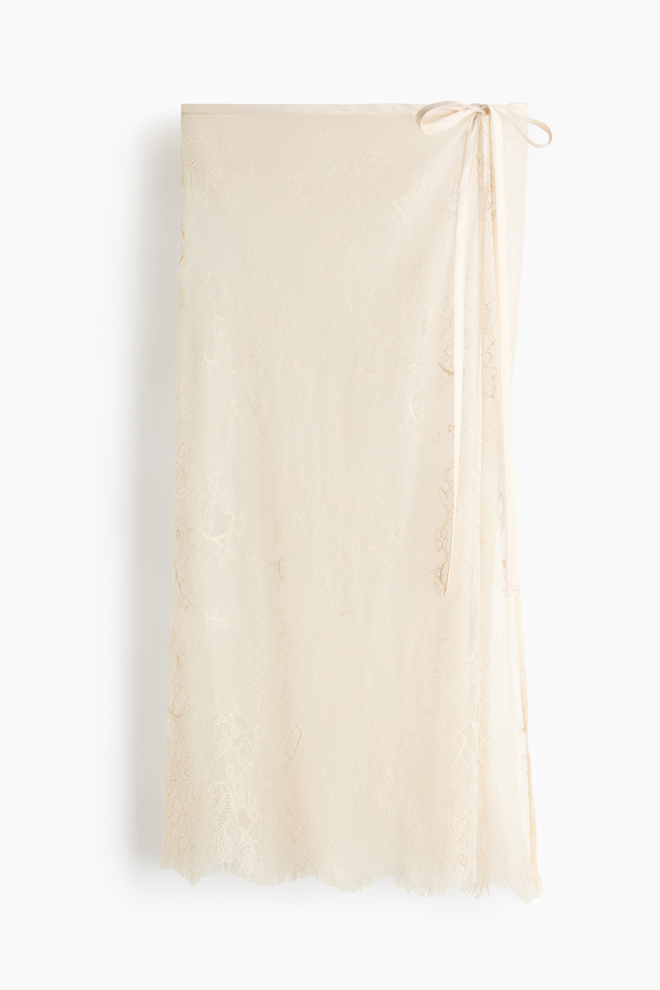 Ver imagen más grande: Una falda envolvente de encaje crema se presenta de frente, con un intrincado patrón floral a lo largo de su tejido translúcido. Se asegura en la parte superior derecha con dos cintas atadas, y su borde inferior muestra un acabado deshilachado y con flecos.