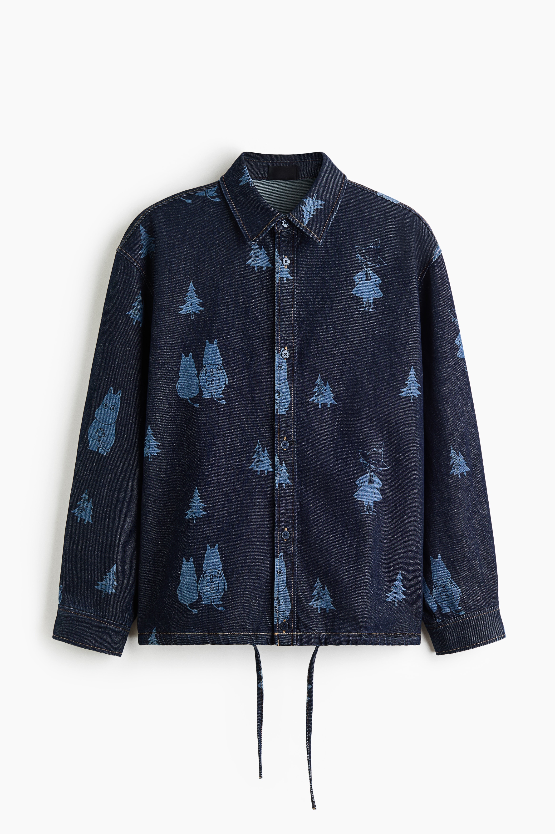 A dark blue denim overshirt featuring a light blue print of cartoon characters and pine trees is being worn by the model. The overshirt features a button-front closure, a classic collar, and dropped shoulders, and is styled with matching printed denim trousers.