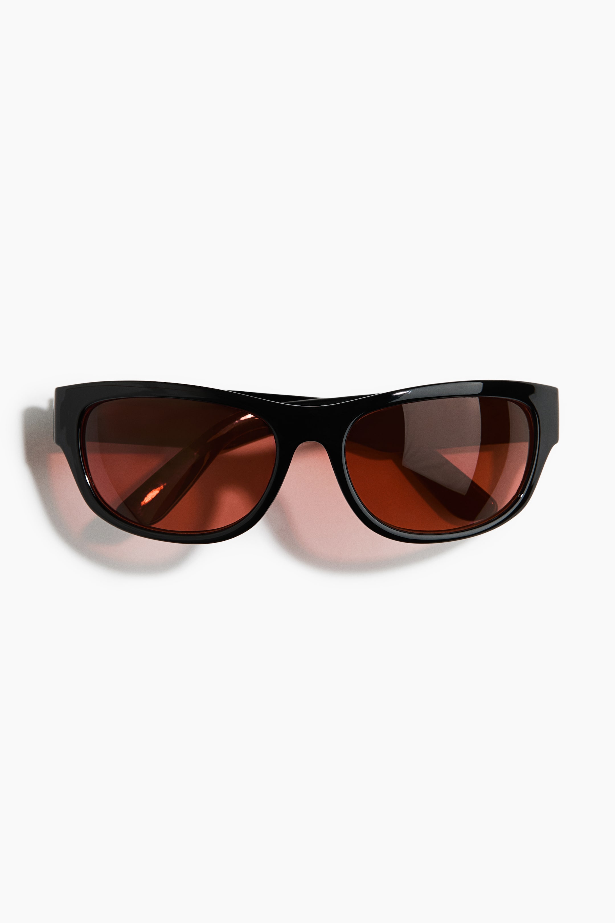 View larger image: Sunglasses feature sleek black frames with a subtle wrap-around design and rich brown lenses.