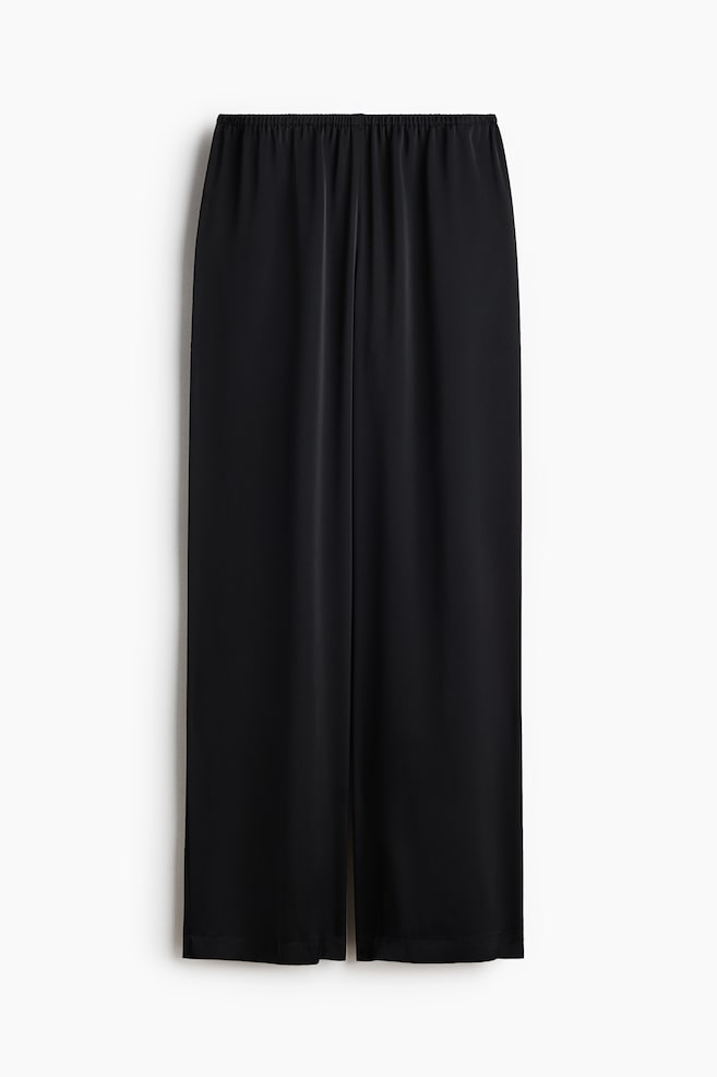 Pantalon noir à coupe ample présenté de face, confectionné dans un tissu satin doux et fluide. La taille est dotée d'une élastication recouverte, et les jambes sont larges. - 1
