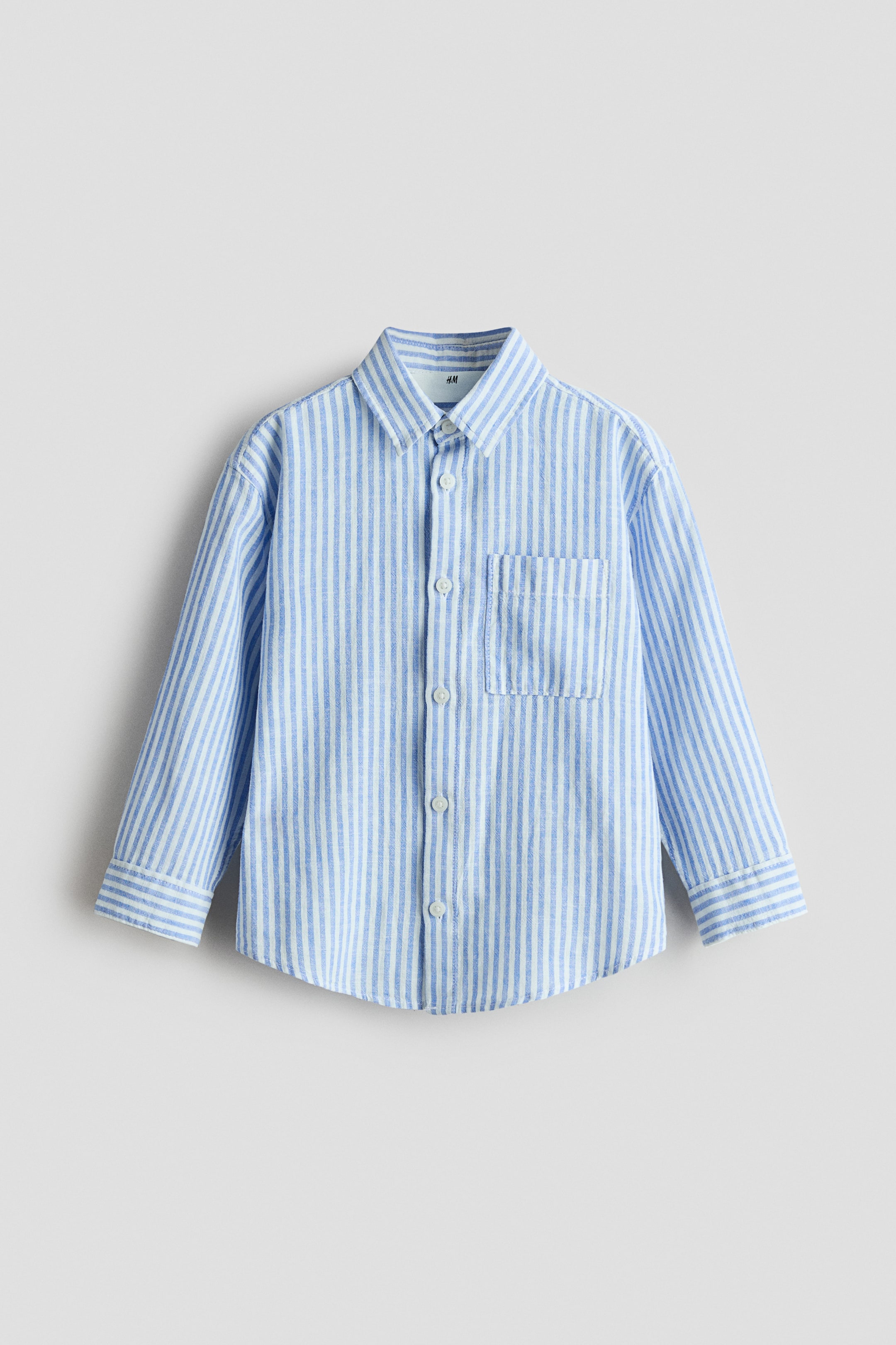 View larger image: This loose-fit shirt is showcased front-facing, featuring a blue and white vertical stripe pattern in a linen and cotton blend. It includes a collar, button-down front, open chest pocket, dropped shoulders, and long sleeves with buttoned cuffs.