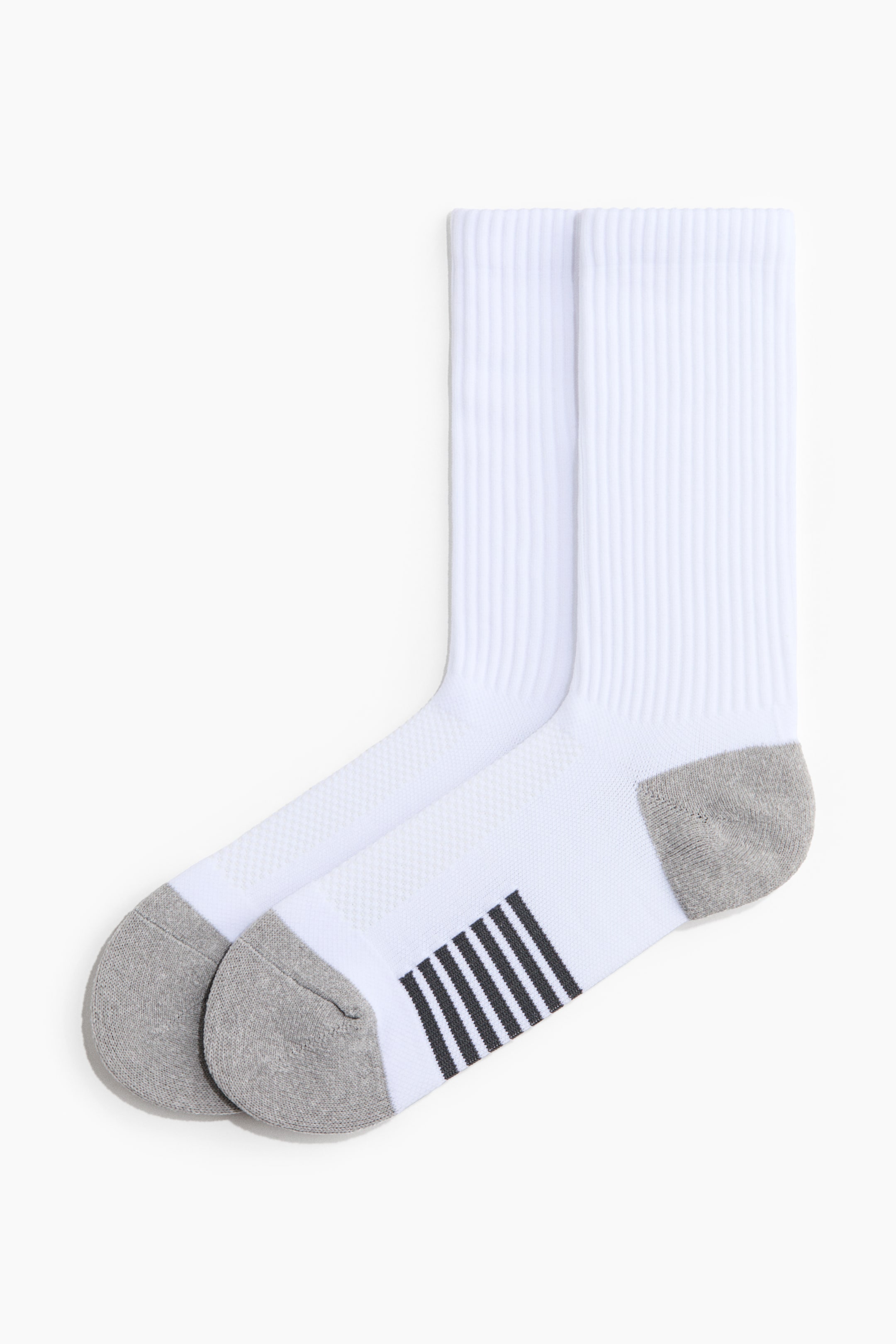 Voir une image plus grande: Une paire de chaussettes de sport blanches est posée côte à côte, avec des tiges côtelées, des talons et des pointes gris, et des rayures noires sur la voûte plantaire. Le dessus du pied présente une texture en maille.