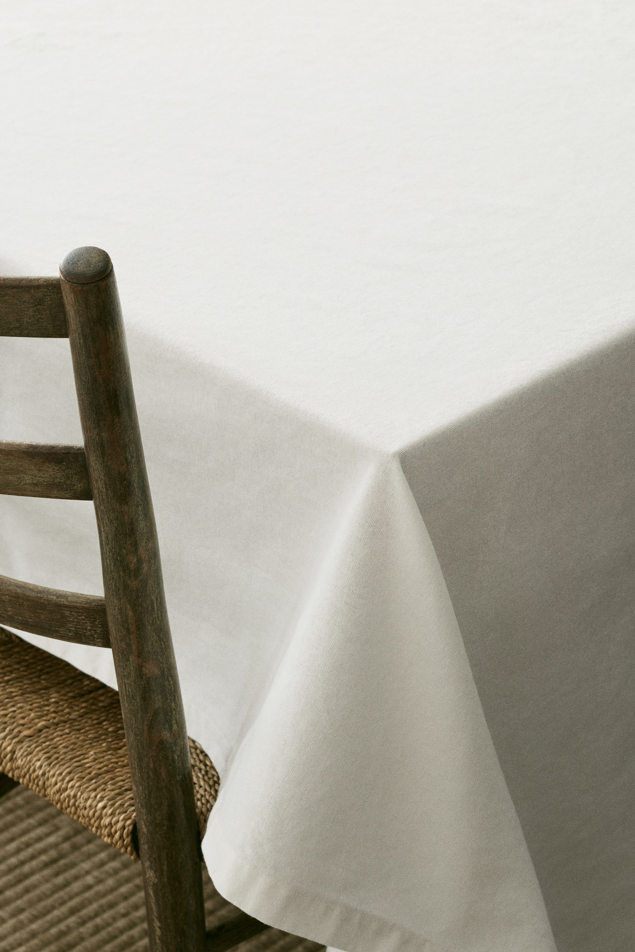 Visualizza l'immagine ingrandita: Una tovaglia leggera color bianco sporco, realizzata in un misto di cotone e lino con una densità di 350 fili, è drappeggiata su un tavolo, mostrando la sua trama visibile. I bordi sono rifiniti con un orlo piegato di 2,5 cm.