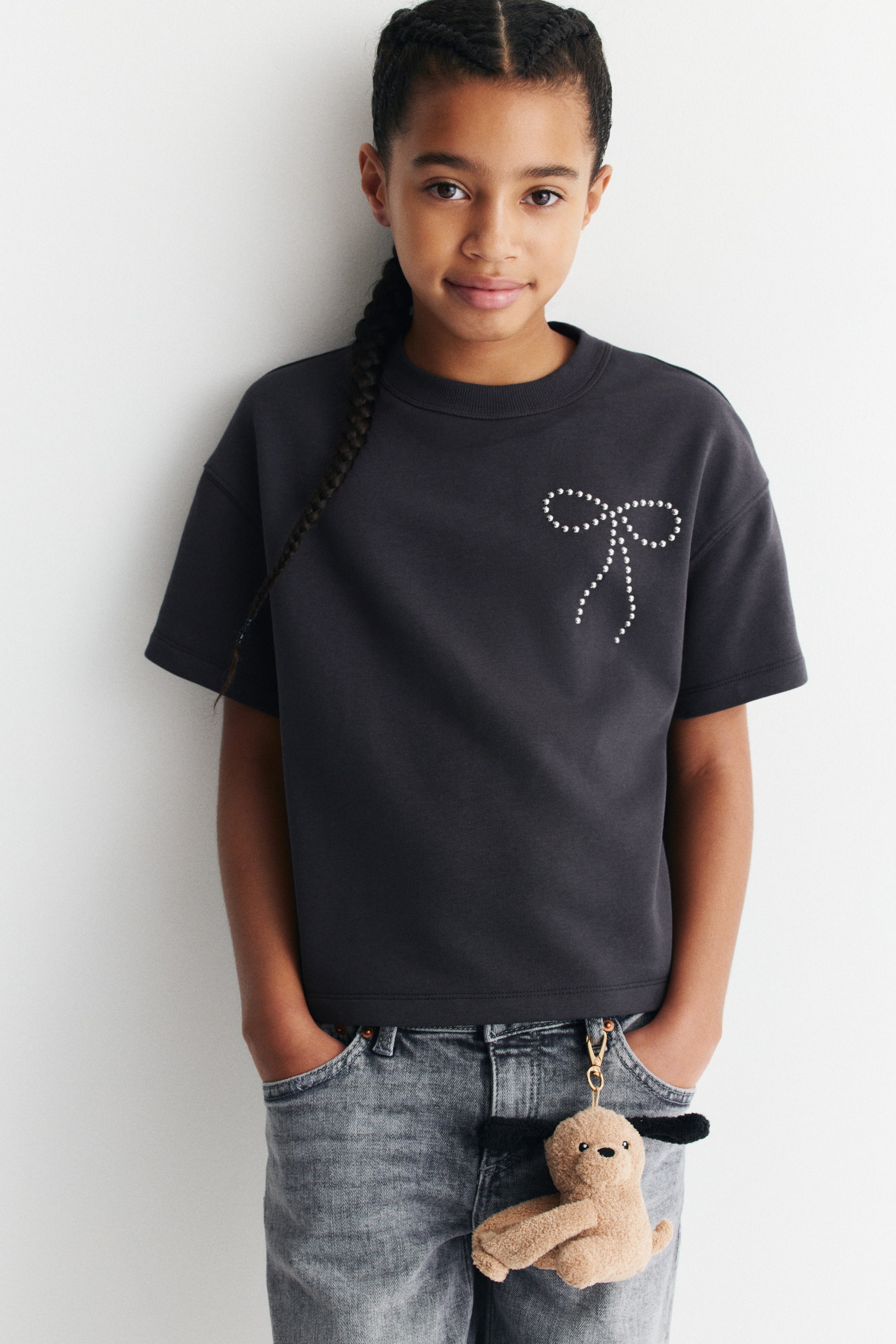 View larger image: A dark gray short-sleeve crew neck t-shirt featuring a white beaded bow design on the front chest.