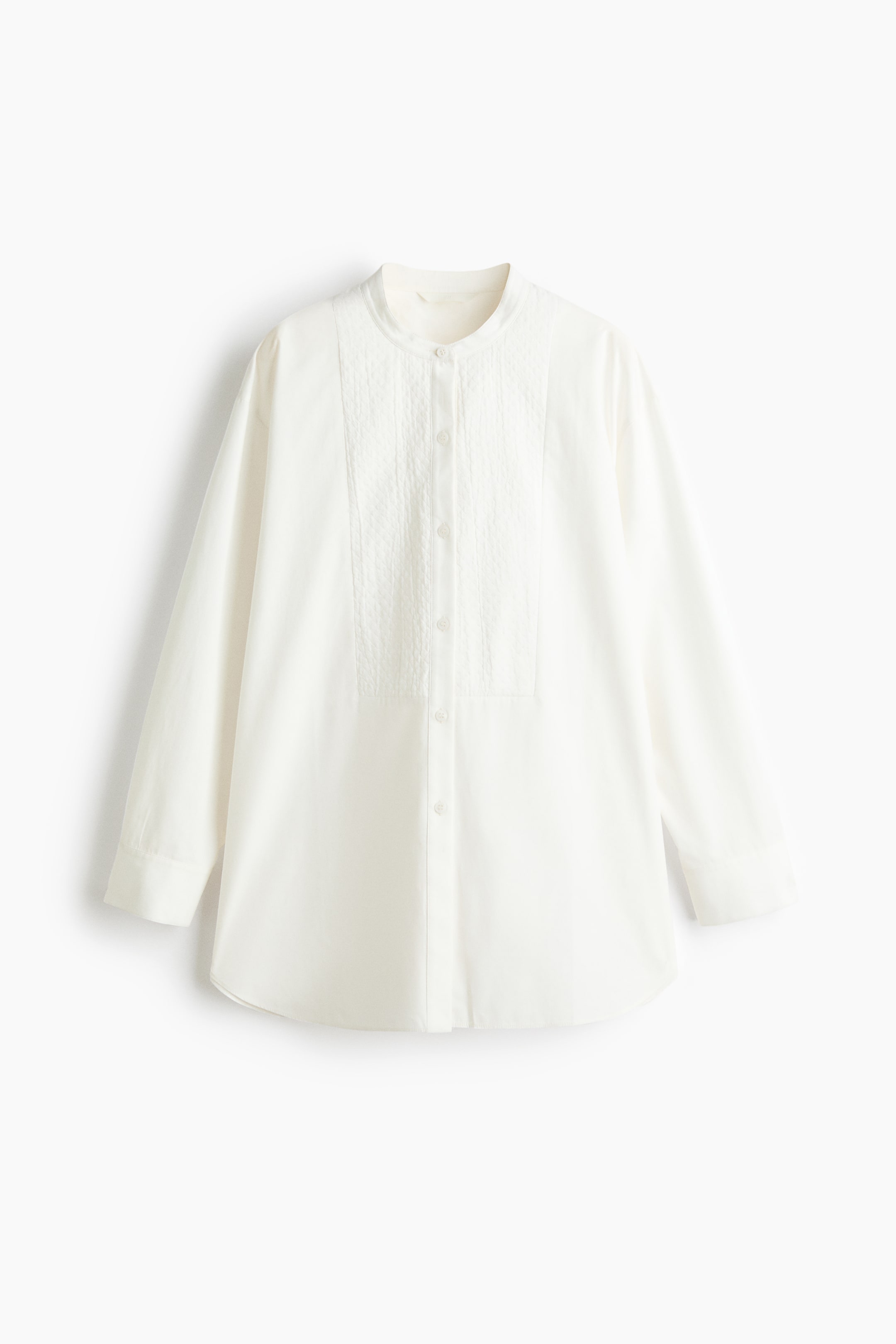 View larger image: A white long-sleeved shirt is shown from the front, featuring a band collar and a textured rectangular bib panel on the chest. The shirt features a button-up front closure, long sleeves with broad cuffs, and a curved hem.
