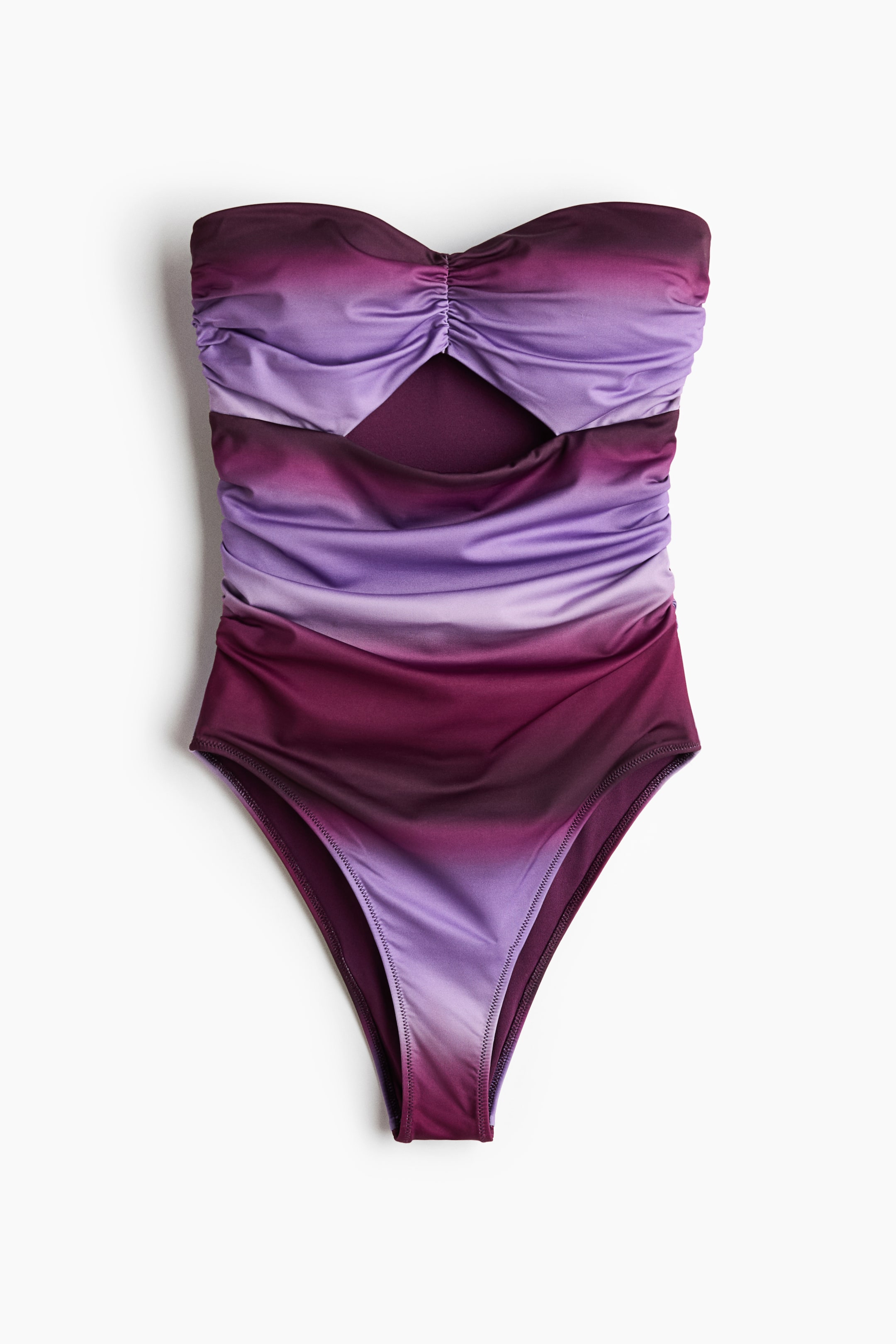 Προβολή μεγαλύτερης εικόνας: Ένα ολόσωμο μαγιό παρουσιάζεται σε μπροστινή όψη, με μοτίβο ombre σε αποχρώσεις μοβ και ματζέντα. Είναι σχεδιασμένο με έναν στράπλες μπαντό τοπ που είναι πλισέ, και ένα τριγωνικό άνοιγμα είναι ορατό κάτω από το στήθος, με επιπλέον πλισέ στο μεσαίο τμήμα.