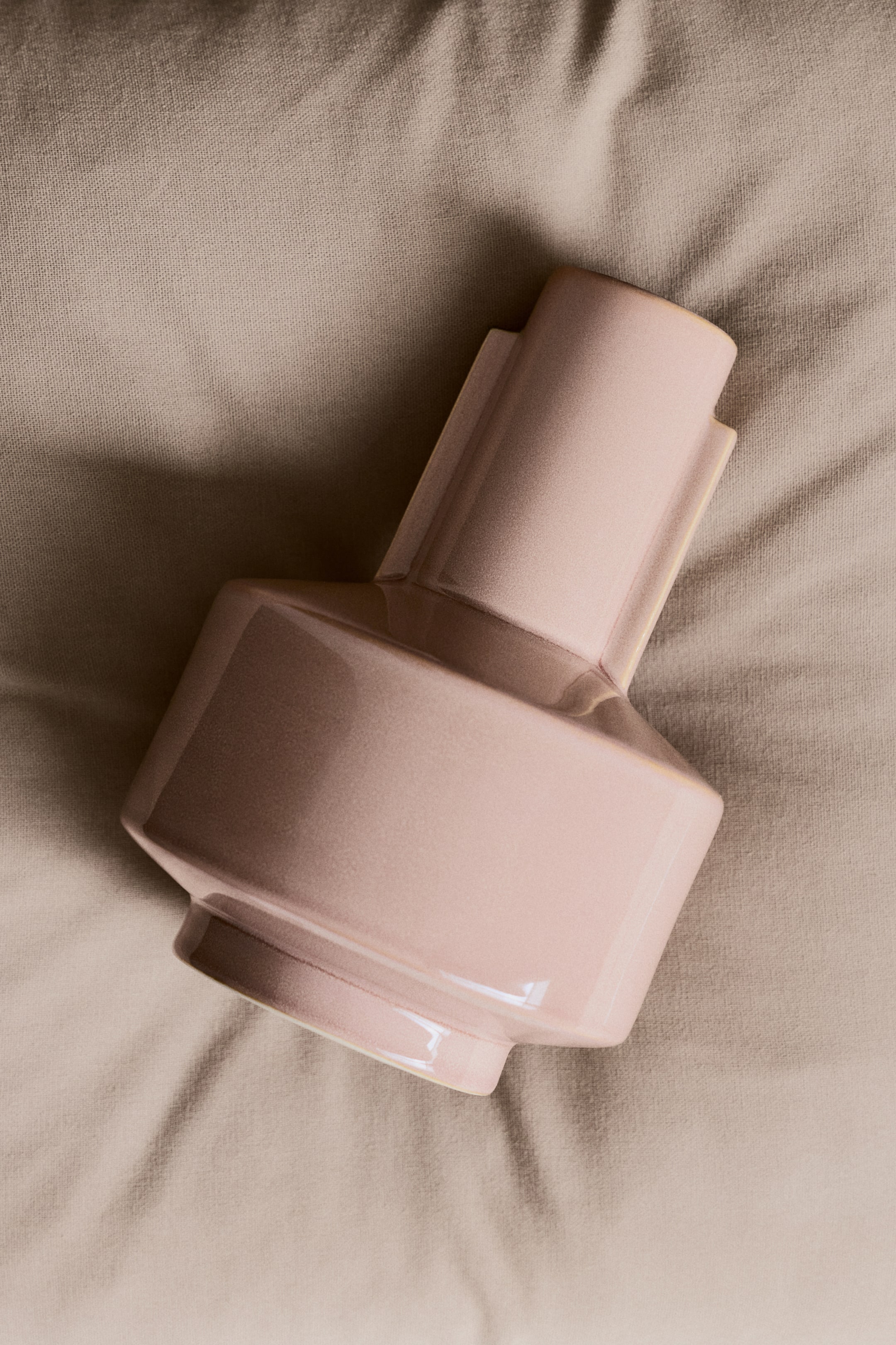 Преглед на по-голямо изображение: Светло розова, лъскава керамична ваза лежи настрани, показваща геометрична структура. Цилиндричната й шийка е с две вертикални, правоъгълни ребра, а фасетираното й тяло се стеснява към ъглова основа.