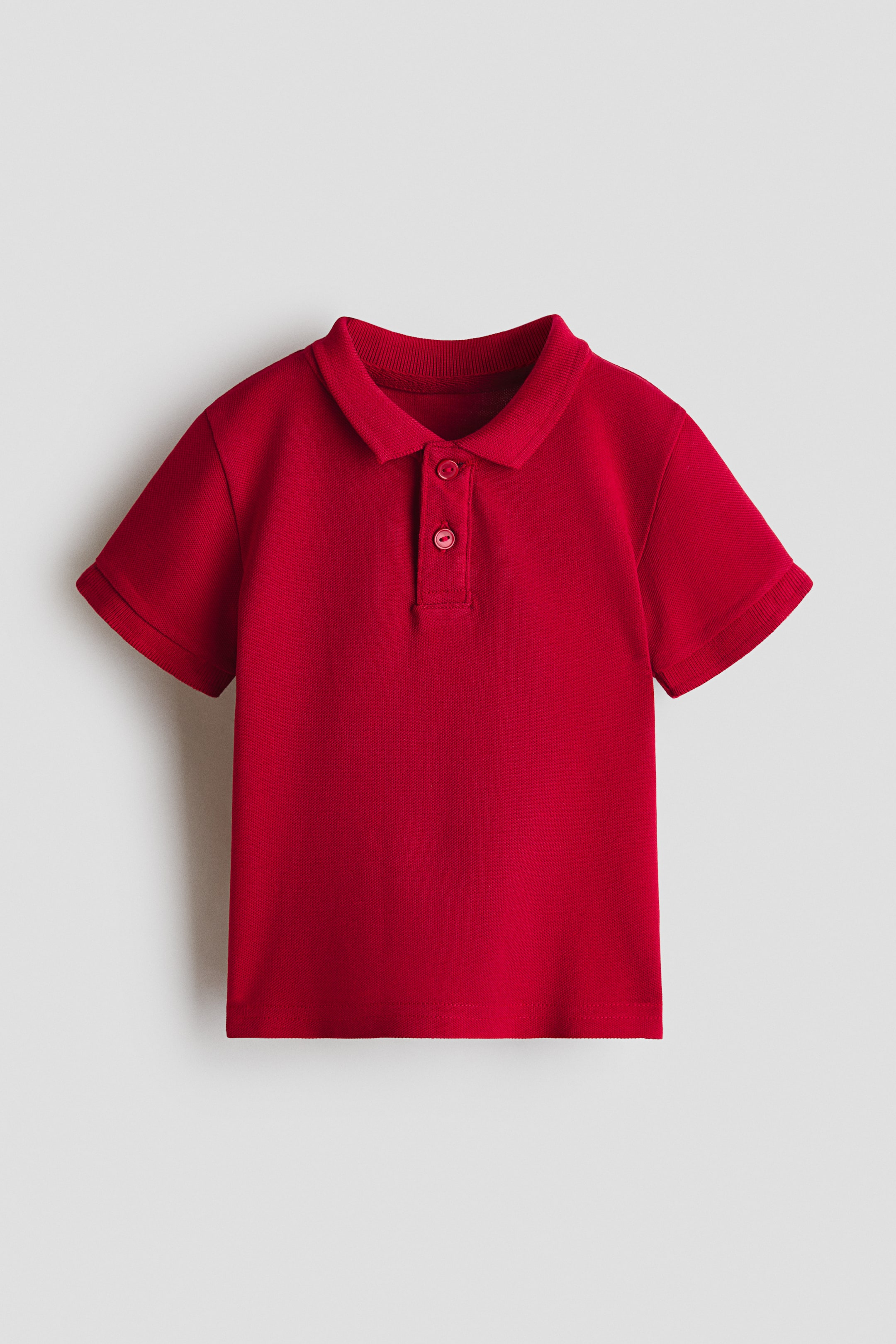View larger image: A red polo shirt featuring a classic polo collar, a two-button placket with matching red buttons, short sleeves with hemmed cuffs, and a piqué knit texture, presented flat and facing forward.
