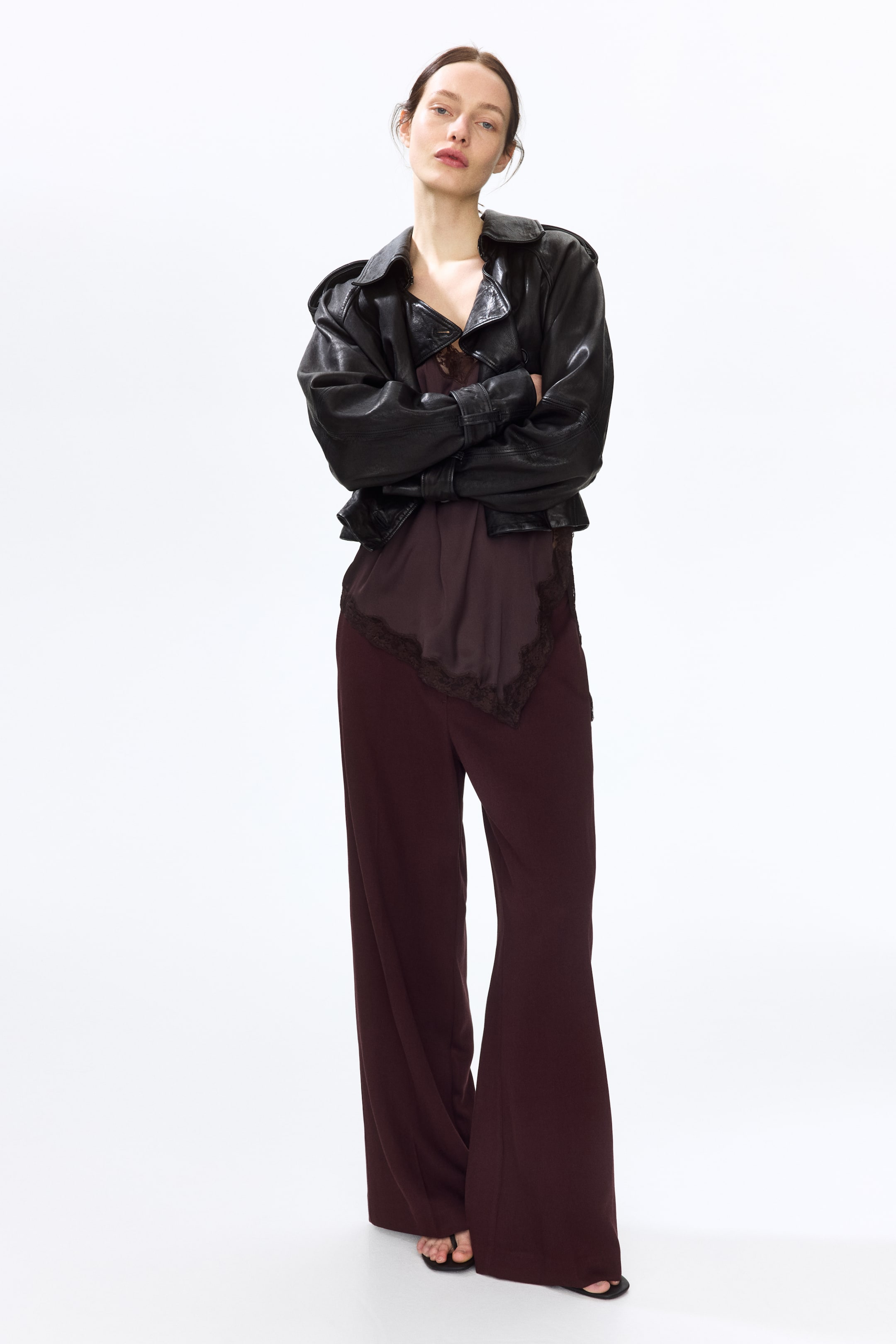 View larger image: The model is wearing tailored, dark red trousers crafted from a woven fabric. These trousers boast a high waist, wide legs, and pronounced creases down the front.